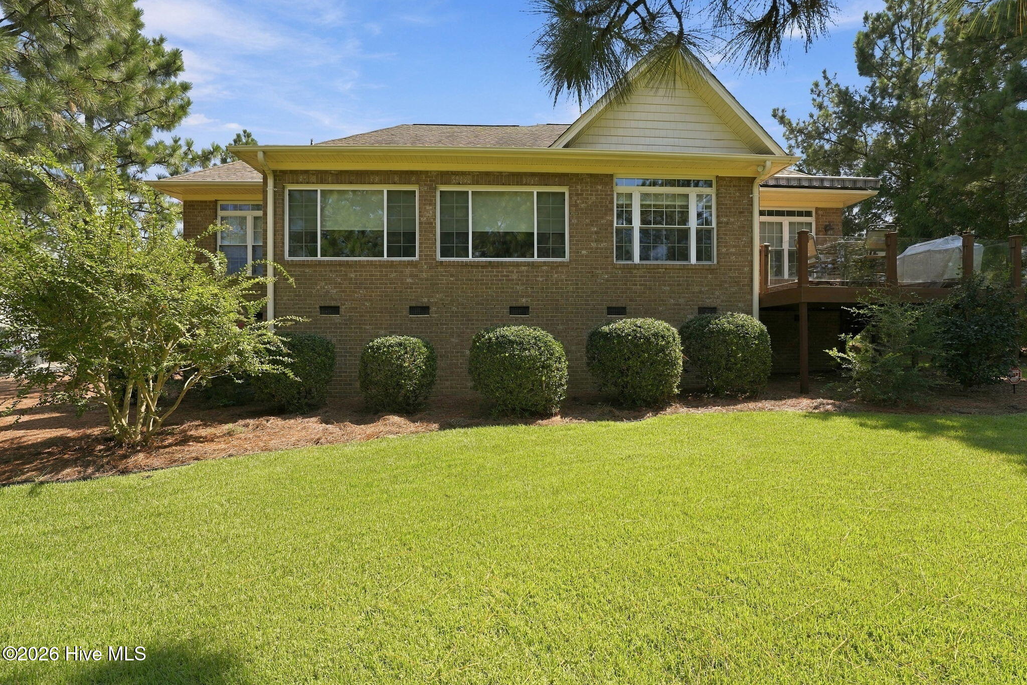 Brick house rear with large windows, a raised deck, trimmed shrubs, and a green lawn.