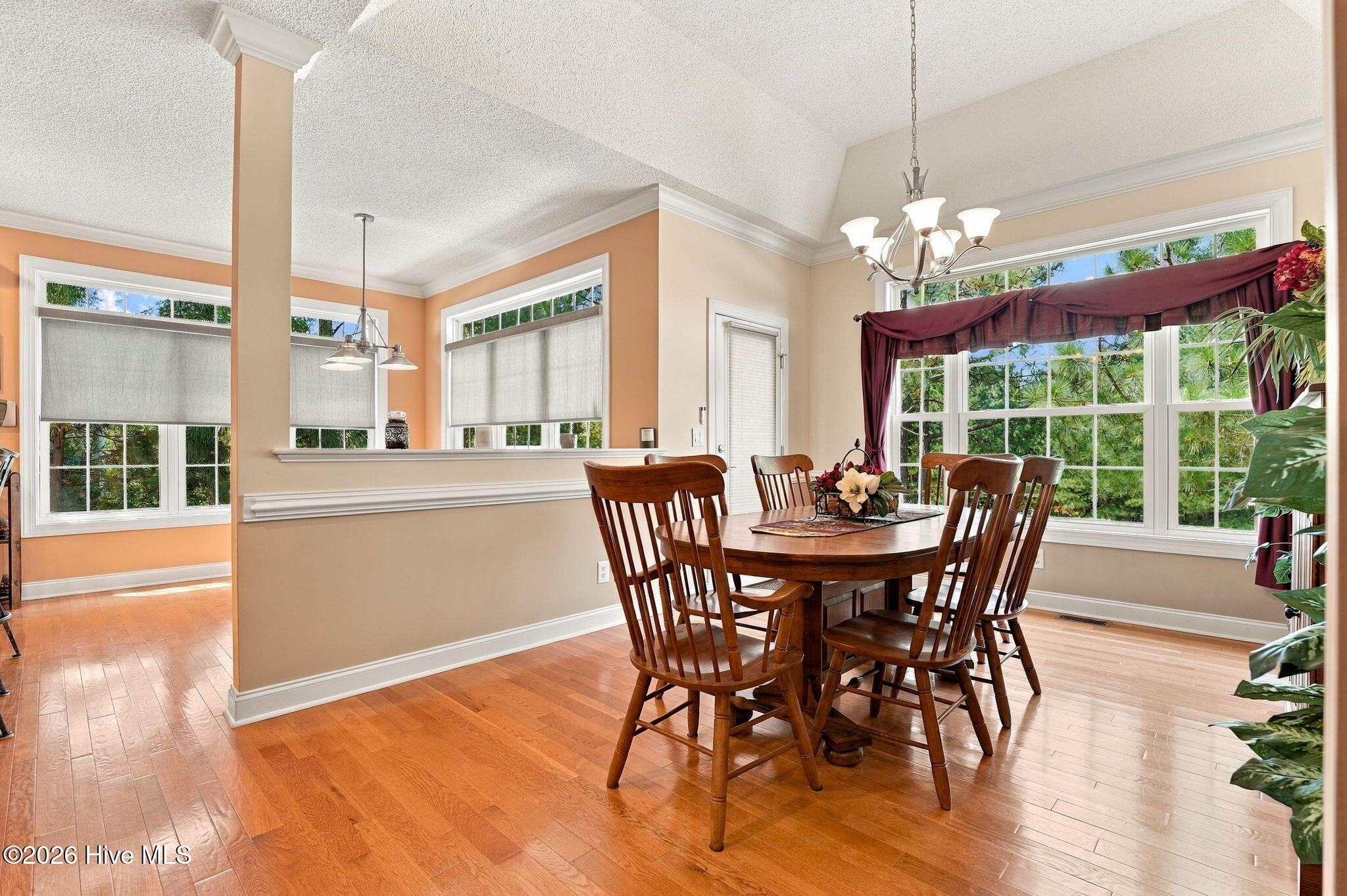 Dining room with a wooden table, hardwood floors, and large windows overlooking trees.