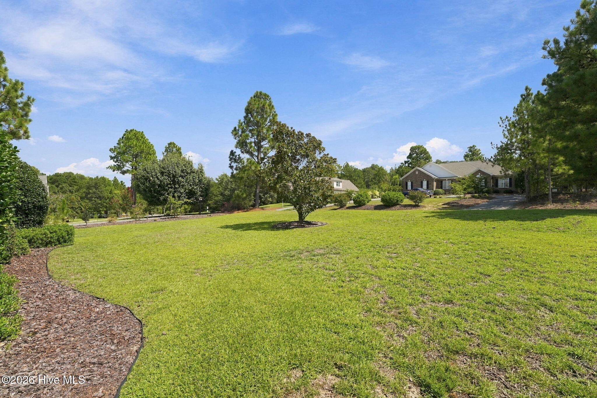 Expansive green lawn with landscaped borders and mature trees leading to a brick home.