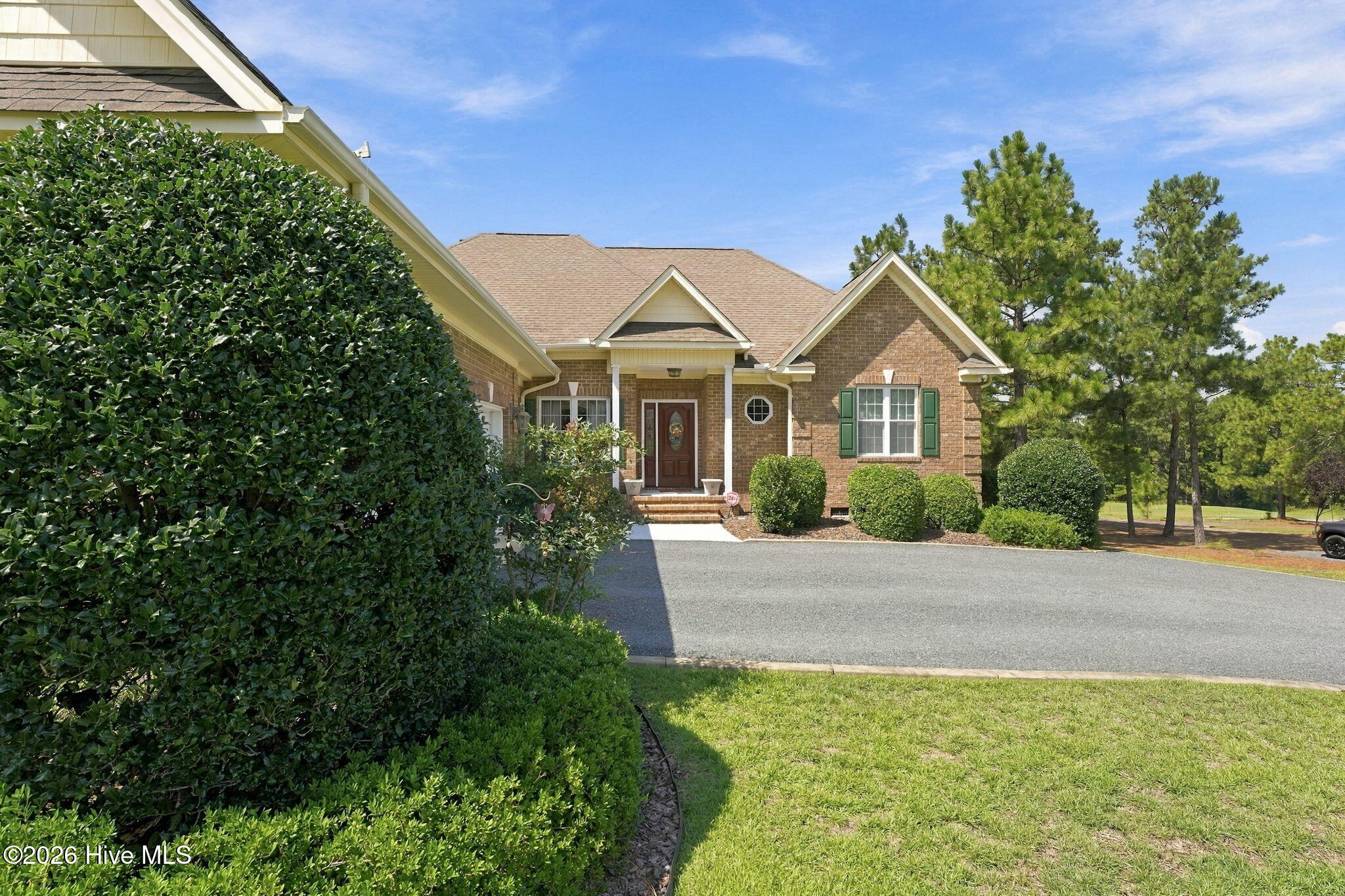 Brick home with a covered front entry, green shutters, trimmed shrubs, and a broad driveway.