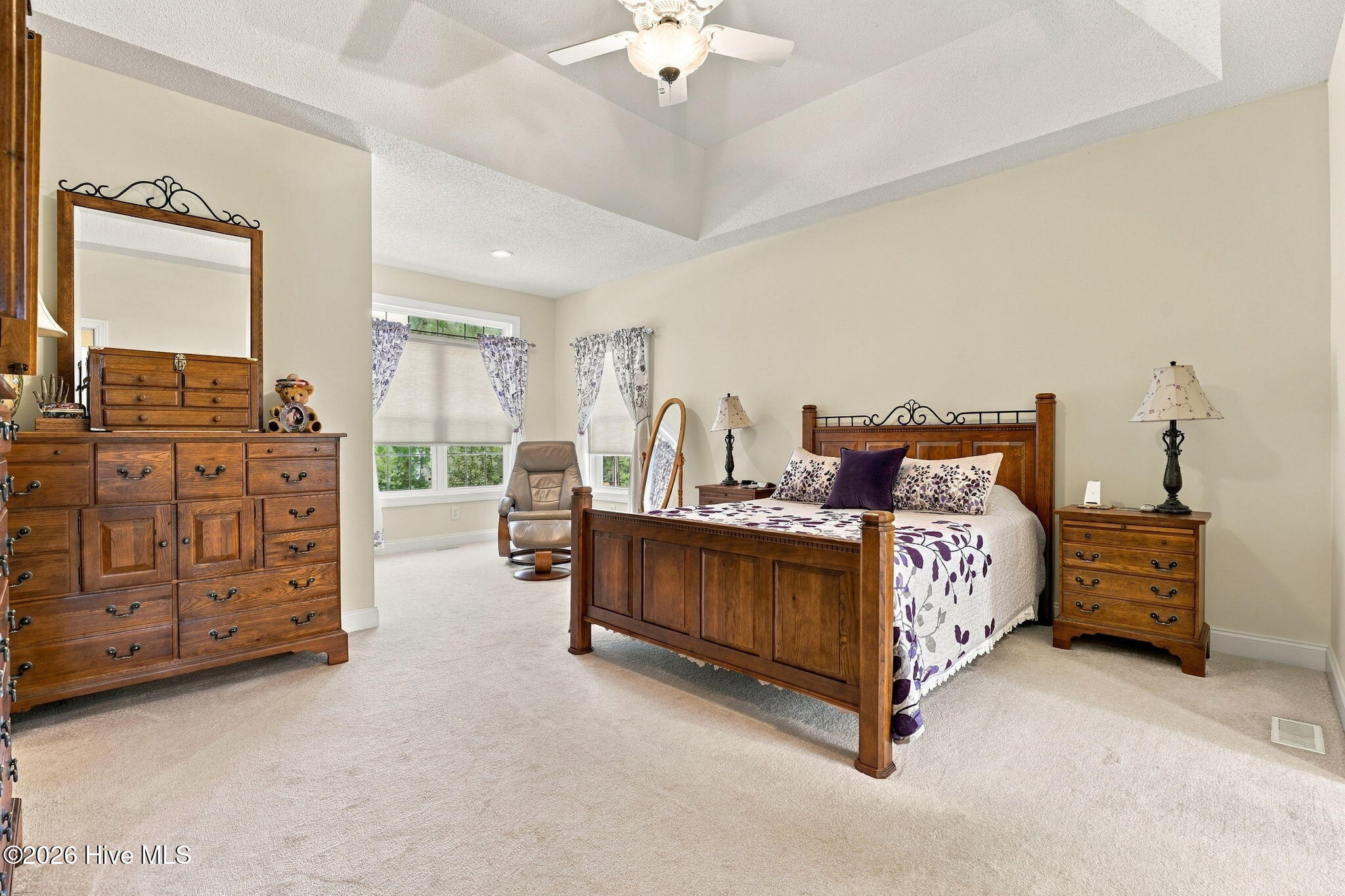 Furnished bedroom with a wood bed, purple floral bedding, matching dressers, and a tray ceiling.