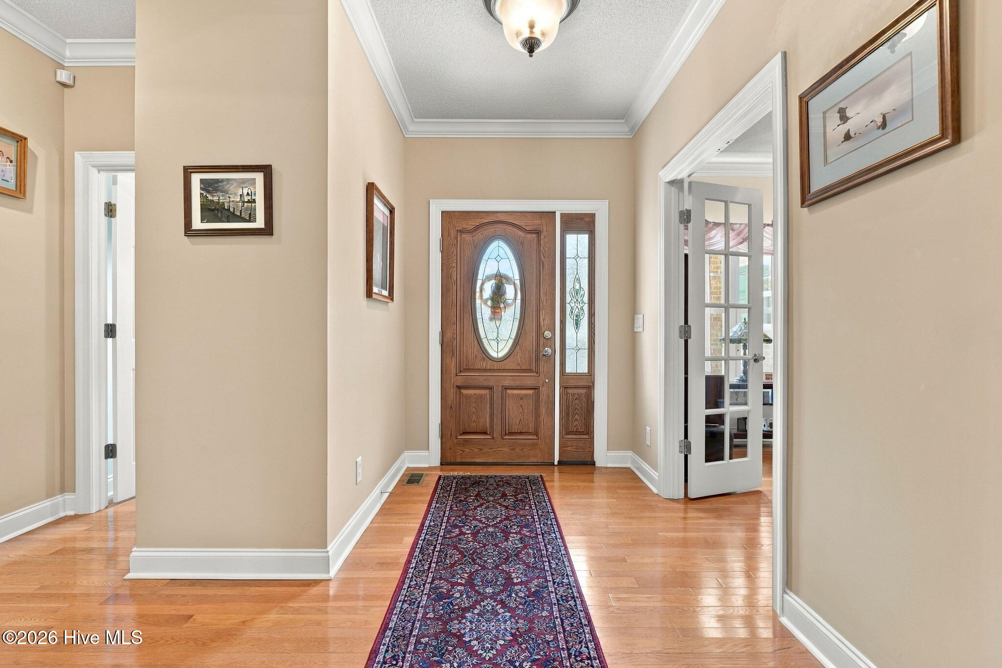 Entry foyer with a glass-paneled wood front door, hardwood floors, and a patterned runner rug.