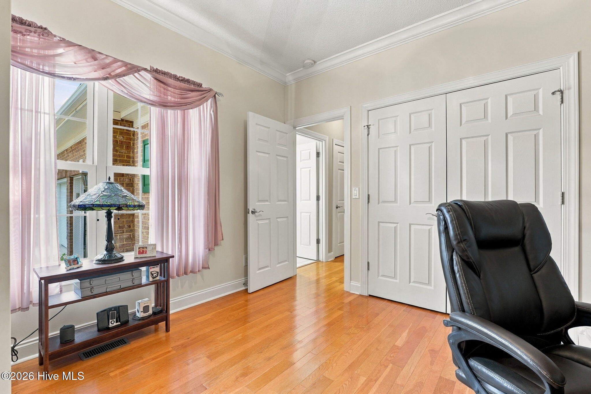 Home office with hardwood floors, white closet doors, and a black leather chair.