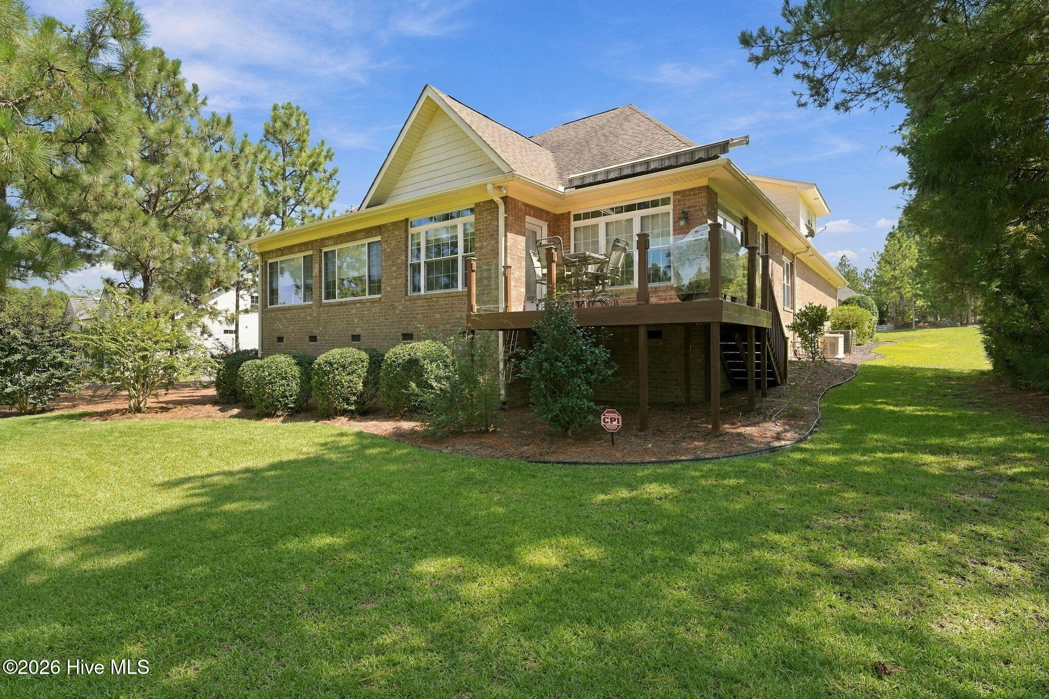 Brick home with raised glass-railed deck and outdoor dining furniture overlooking a broad lawn.