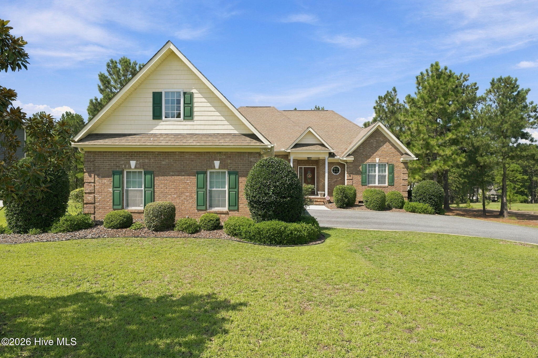 Brick house with cream gables, green shutters, trimmed shrubs, and a broad front lawn.