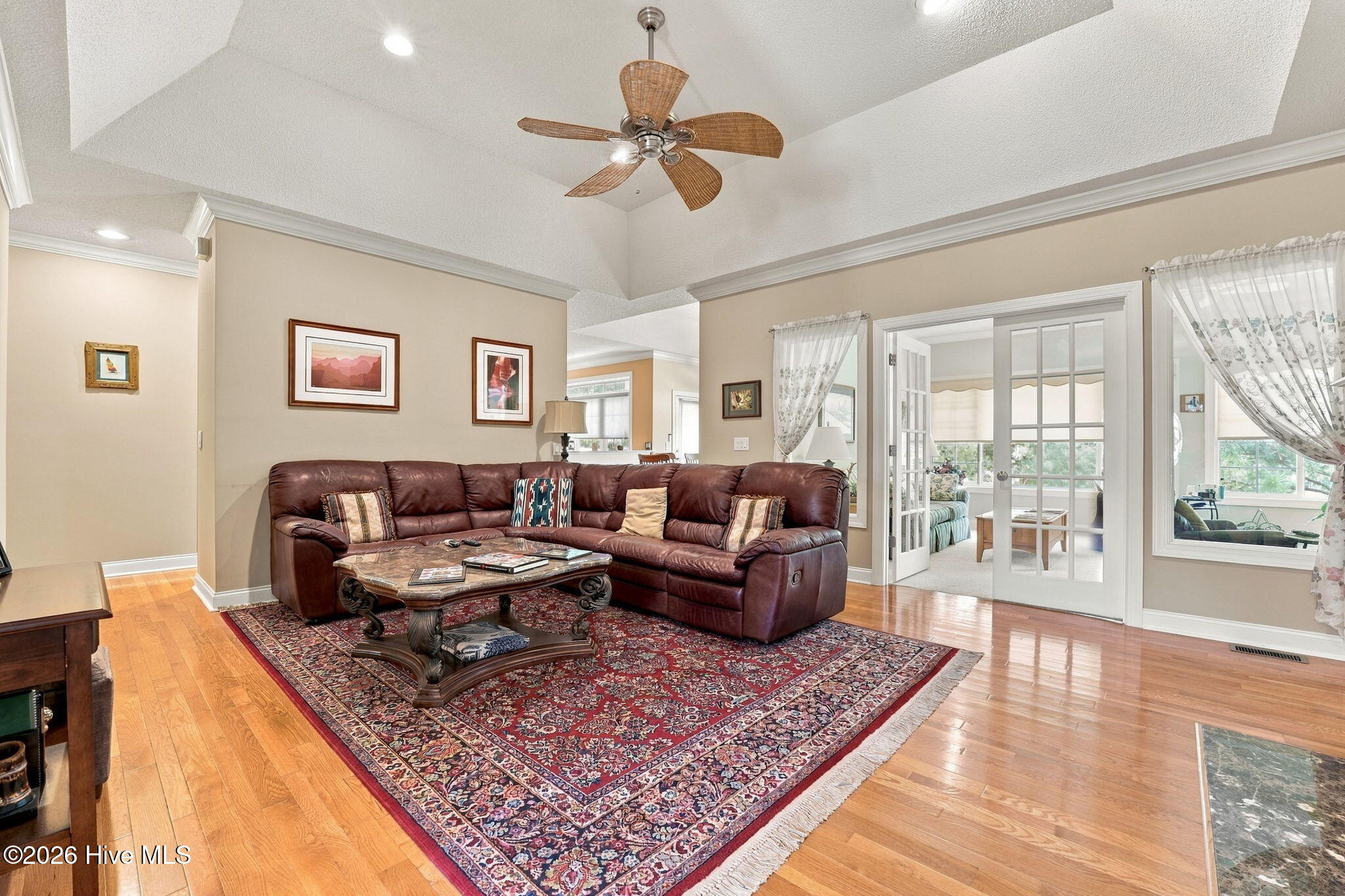 Living room with vaulted ceiling, burgundy leather sectional, patterned rug, and French doors to a sitting room.