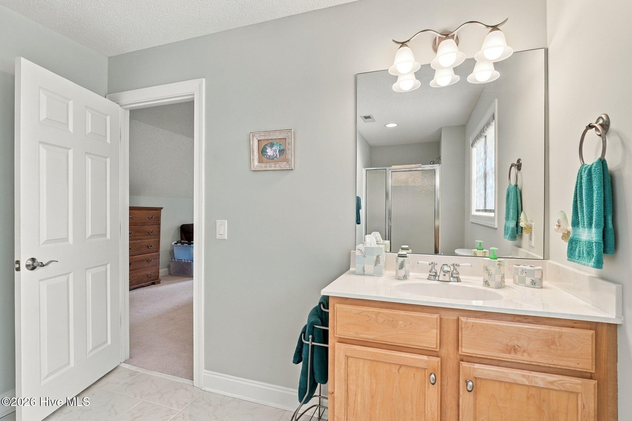Bathroom with a light wood double vanity, broad mirror, and glass-enclosed shower.