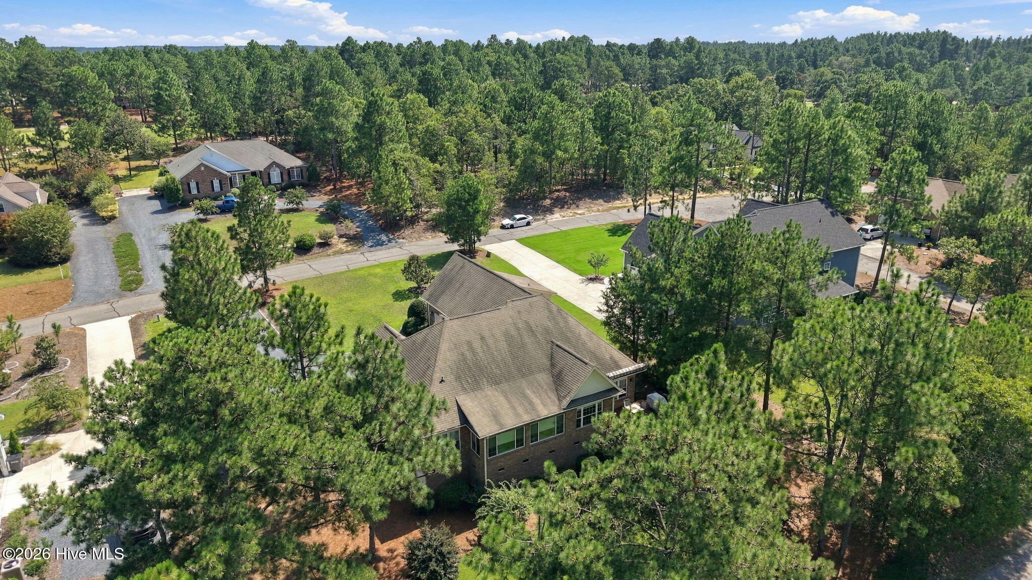 Aerial view of a brick home among pine trees, neighboring houses, and landscaped yards.