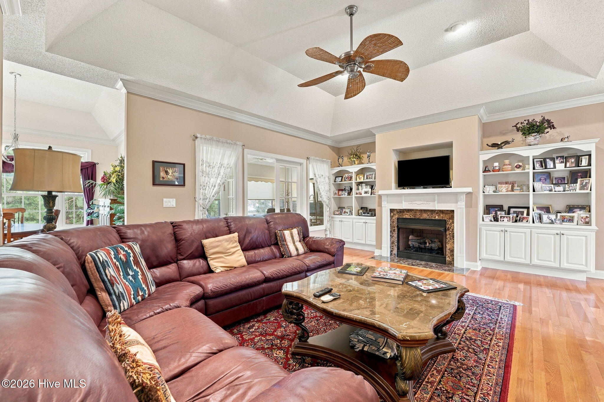 Living room with a burgundy leather sectional, fireplace, built-in shelving, and tray ceiling.