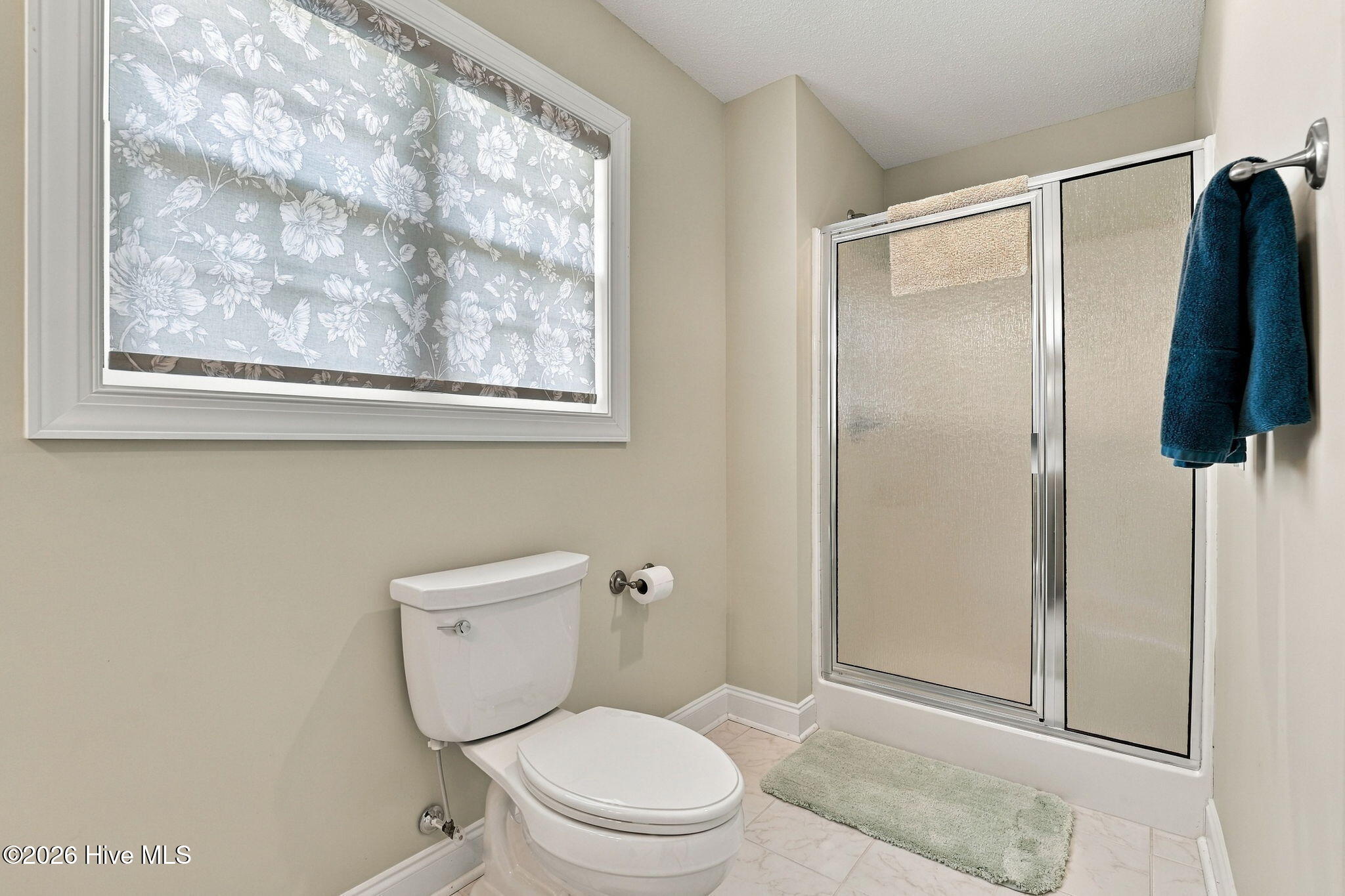 Bathroom with a glass shower, white toilet, and floral Roman shade.