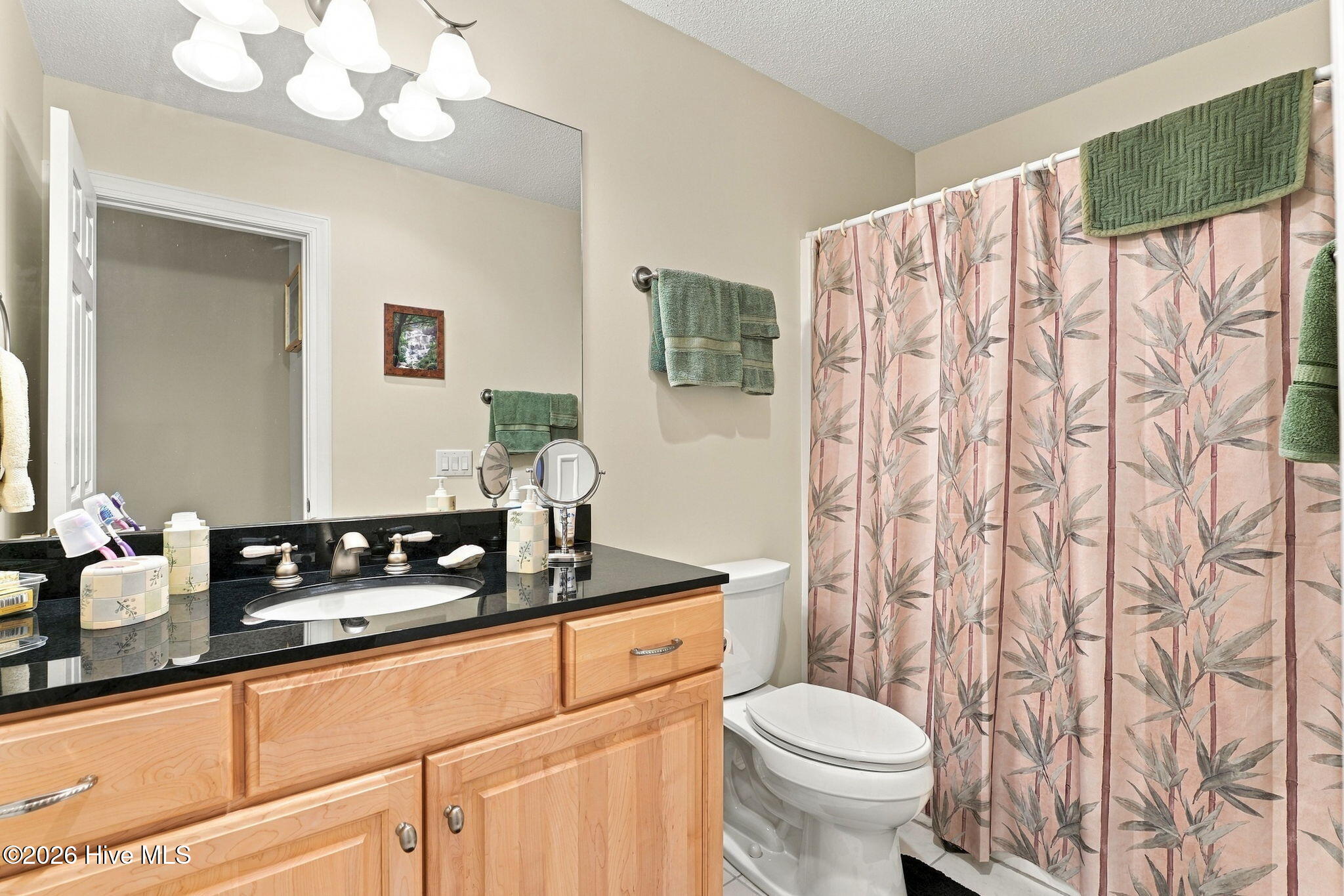 Bathroom with a light wood vanity and black countertop beside a toilet and pink bamboo-pattern shower curtain.