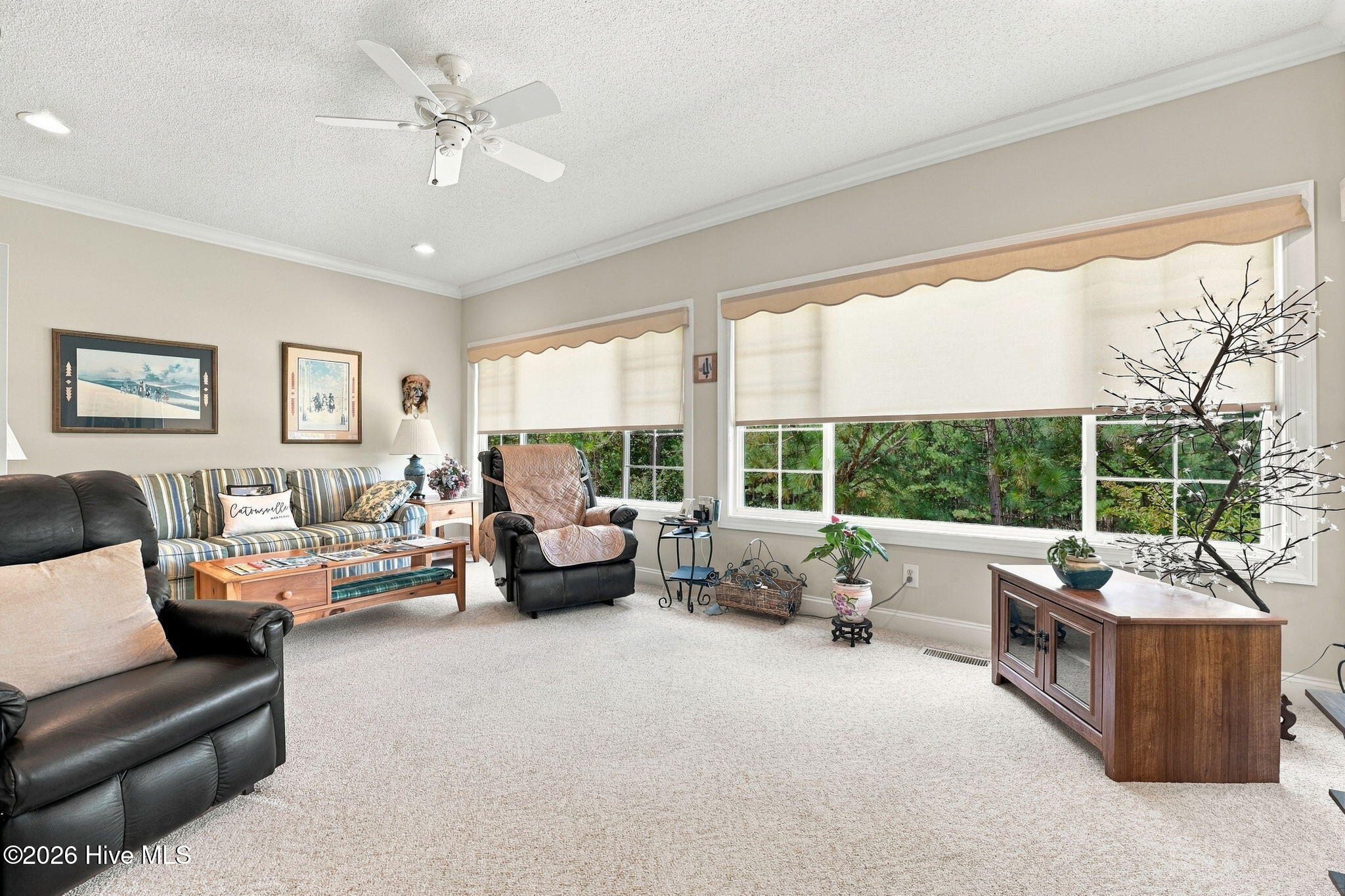 Furnished living room with a striped sofa, leather recliners, and large windows overlooking trees.