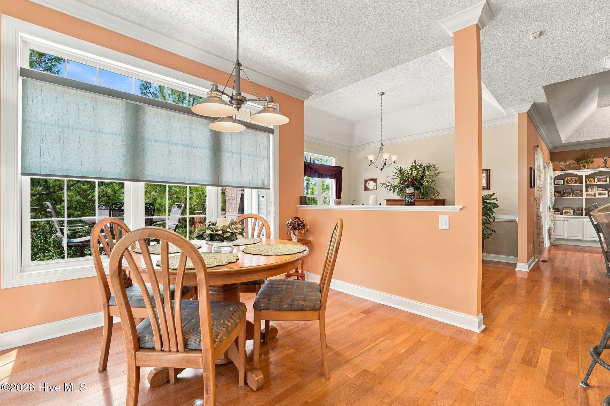 Dining room with a round wooden table beside a large window overlooking greenery.