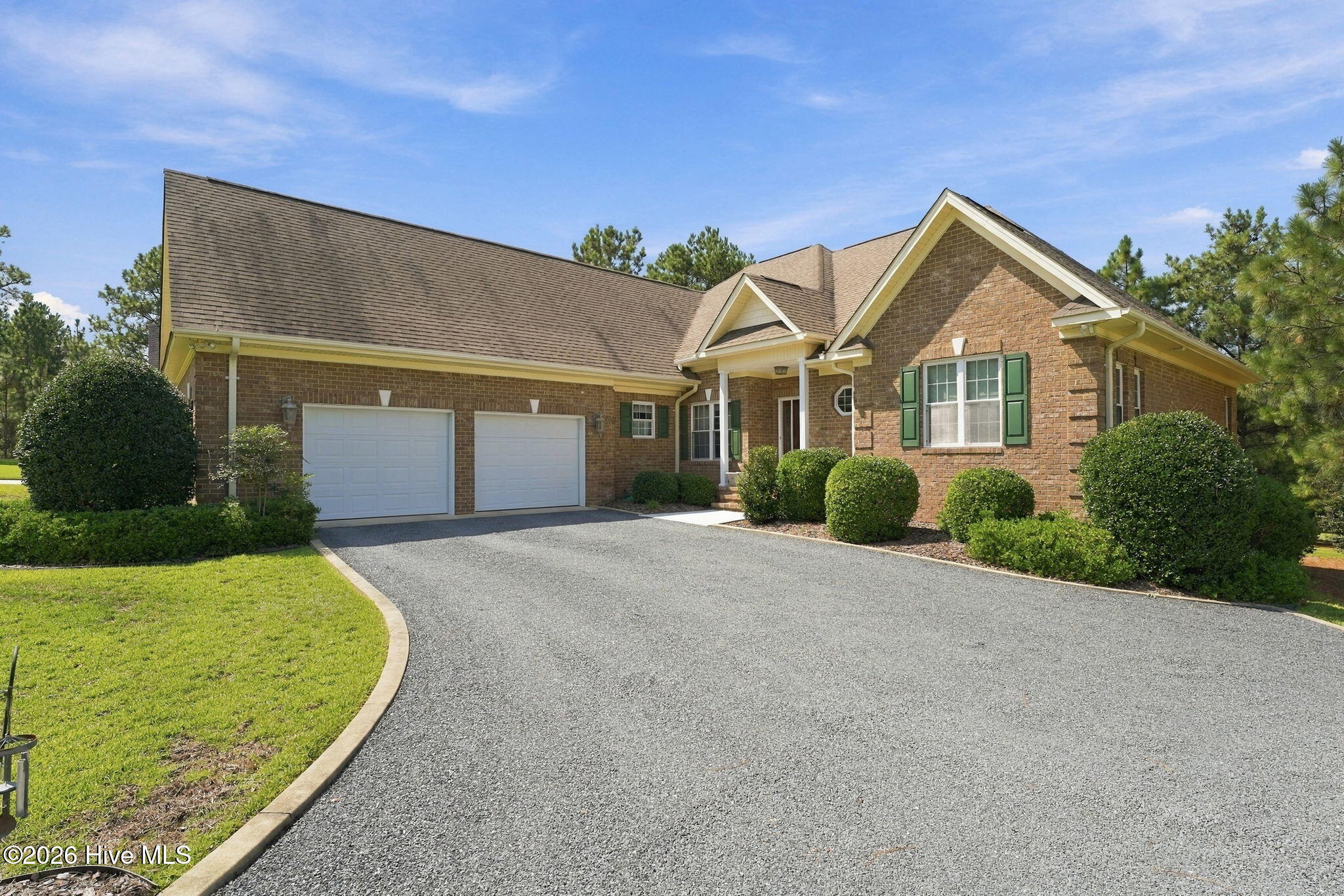 Brick house with green shutters, two-car garage, and broad gravel driveway.