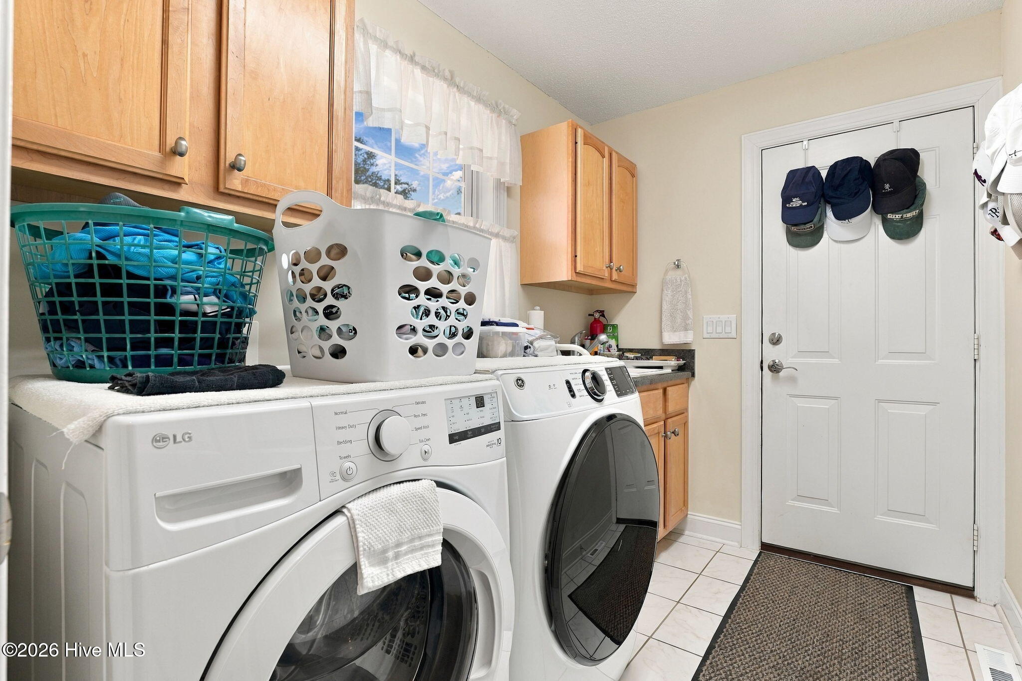 Laundry room with front-loading washer and dryer, wooden cabinets, and a window above the machines.