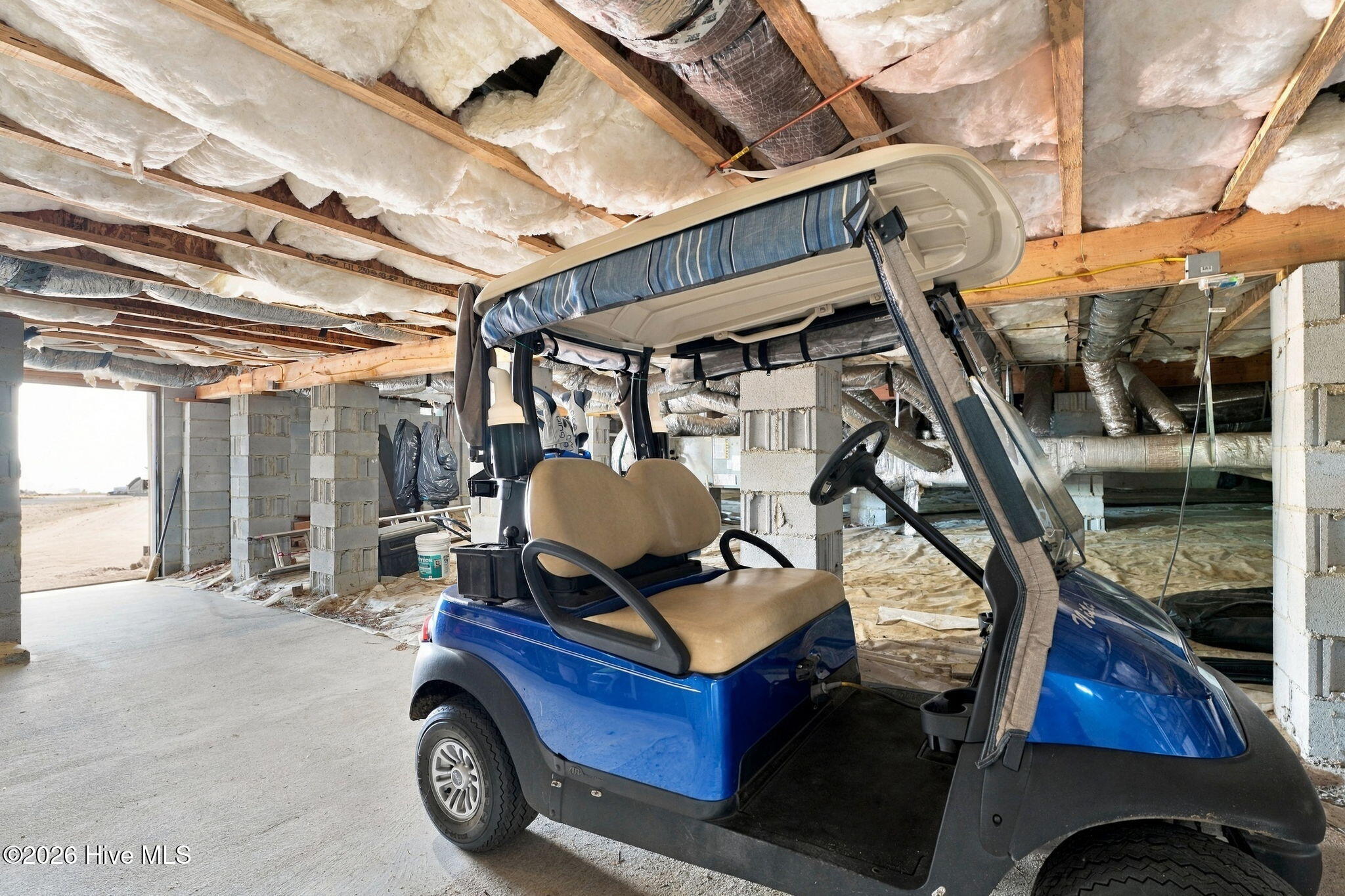 Unfinished insulated garage with a blue golf cart parked beneath exposed ceiling joists.