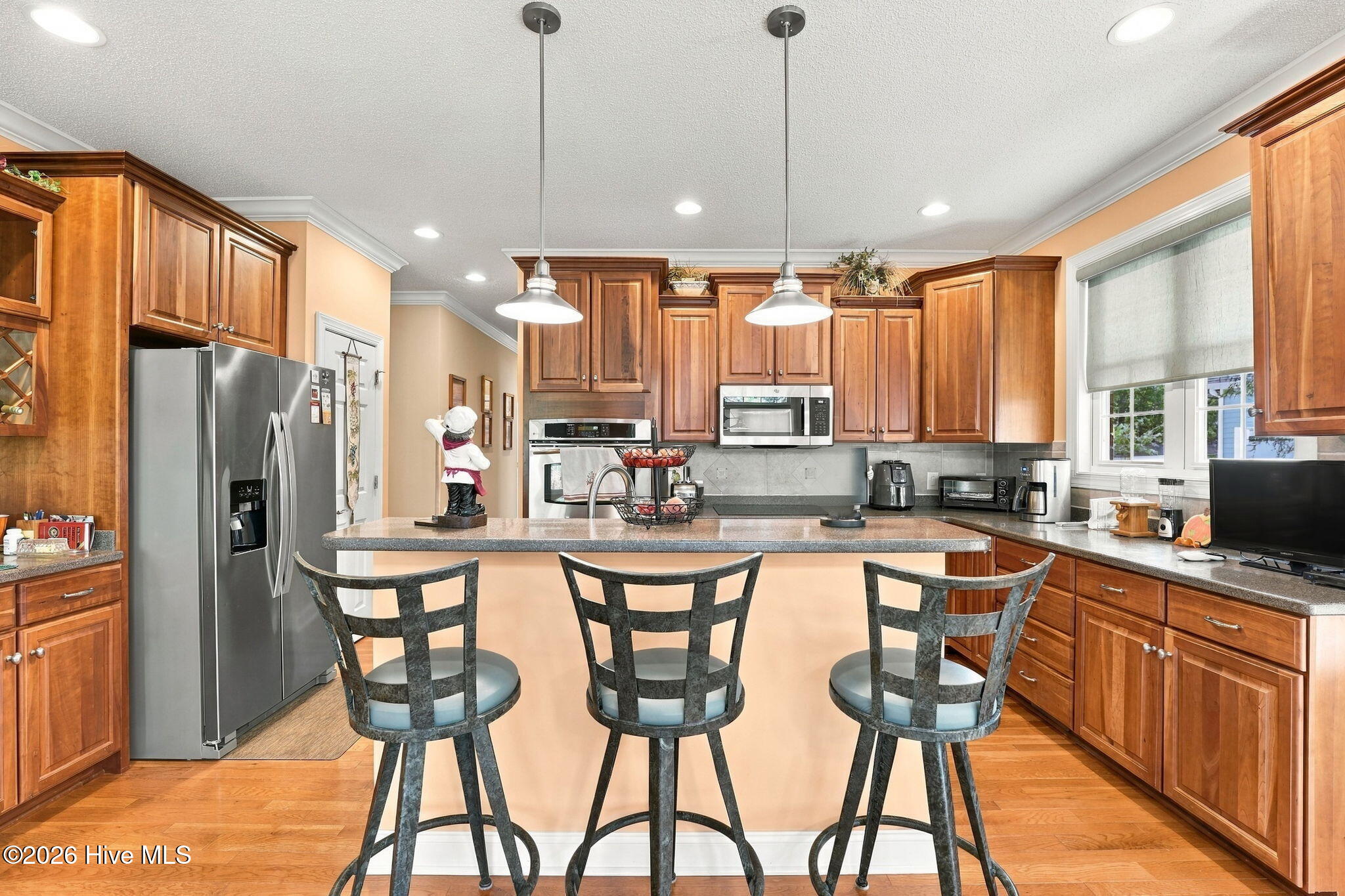 Kitchen with extensive wood cabinetry, stainless steel appliances, and a large island with three bar stools.