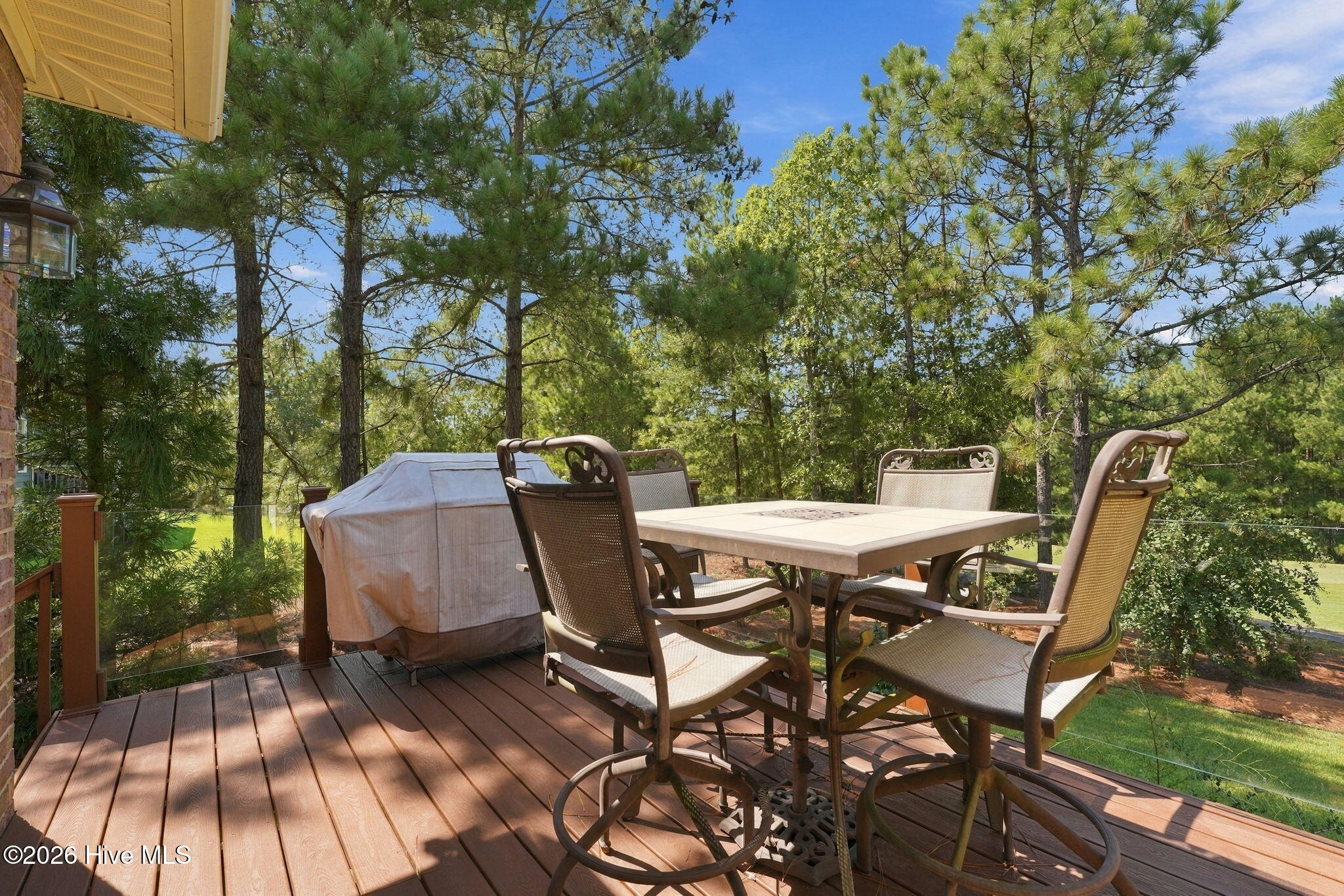 Furnished deck with patio dining set and covered grill overlooking trees.