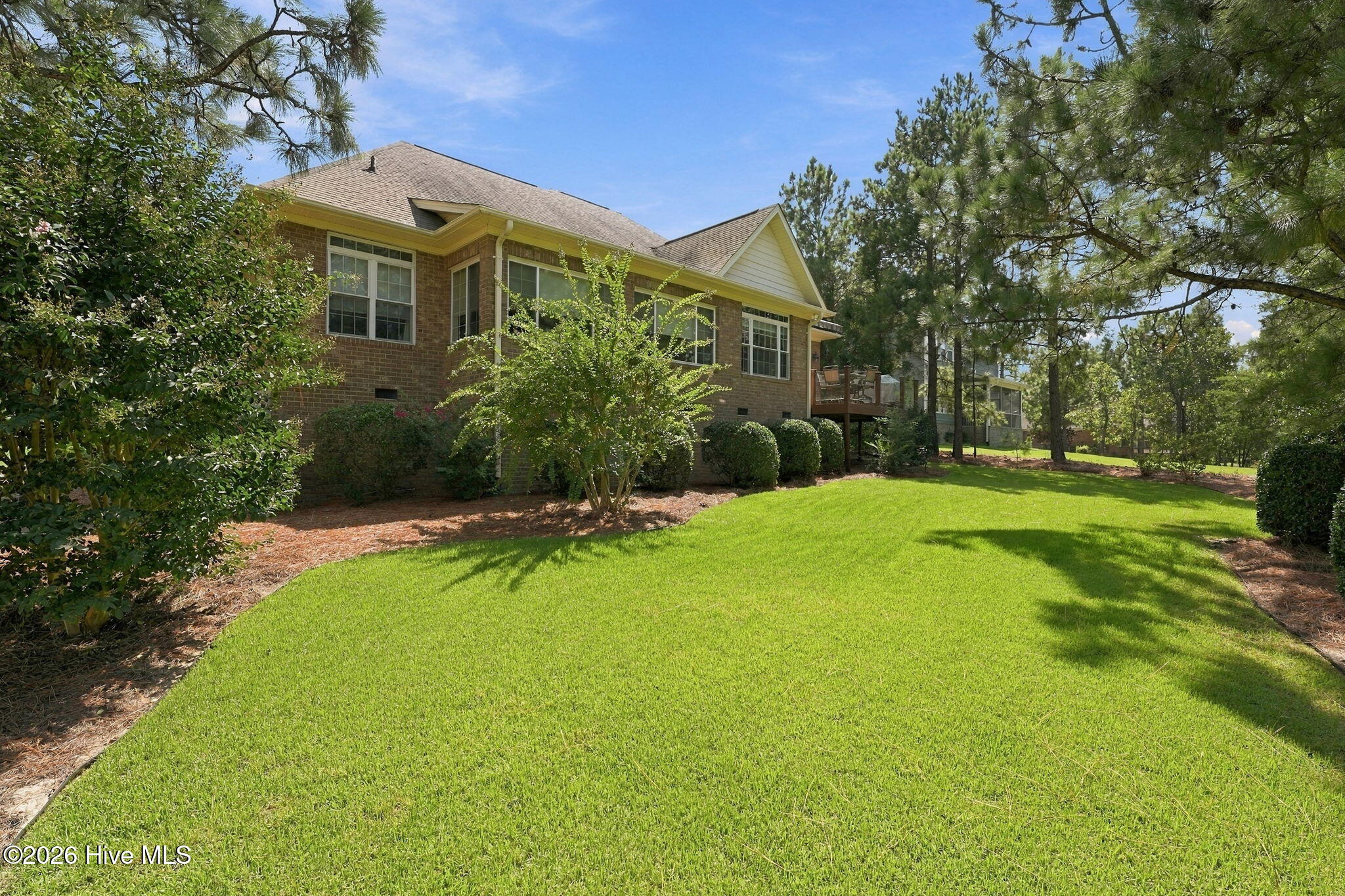 Brick house rear exterior with a raised deck and a broad, tree-shaded lawn.