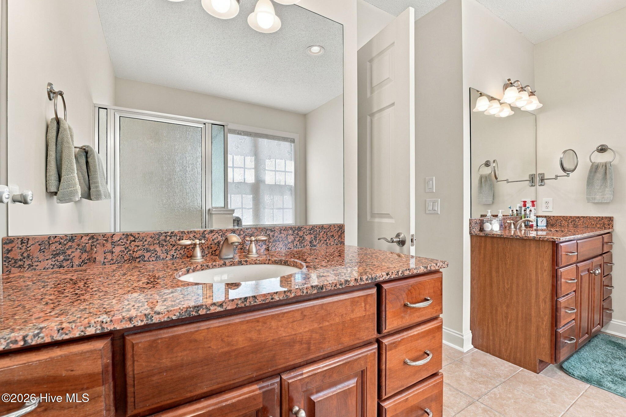 Bathroom with dual wood vanities and granite countertops beside a frosted-glass shower.