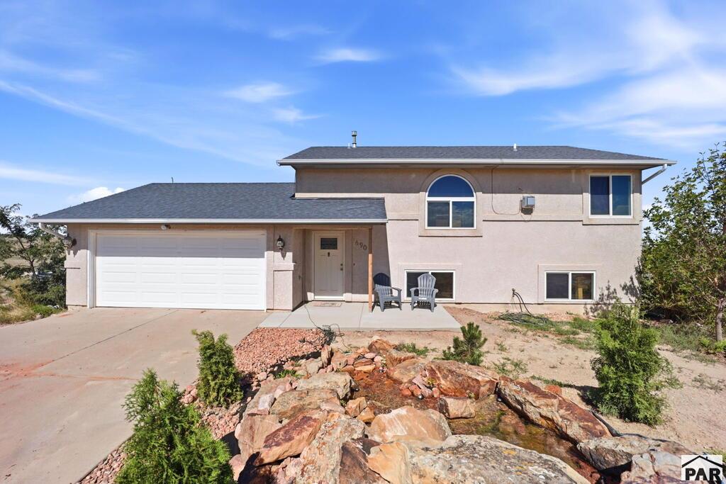 Beige stucco home with an attached garage, arched window, and rock landscaping.