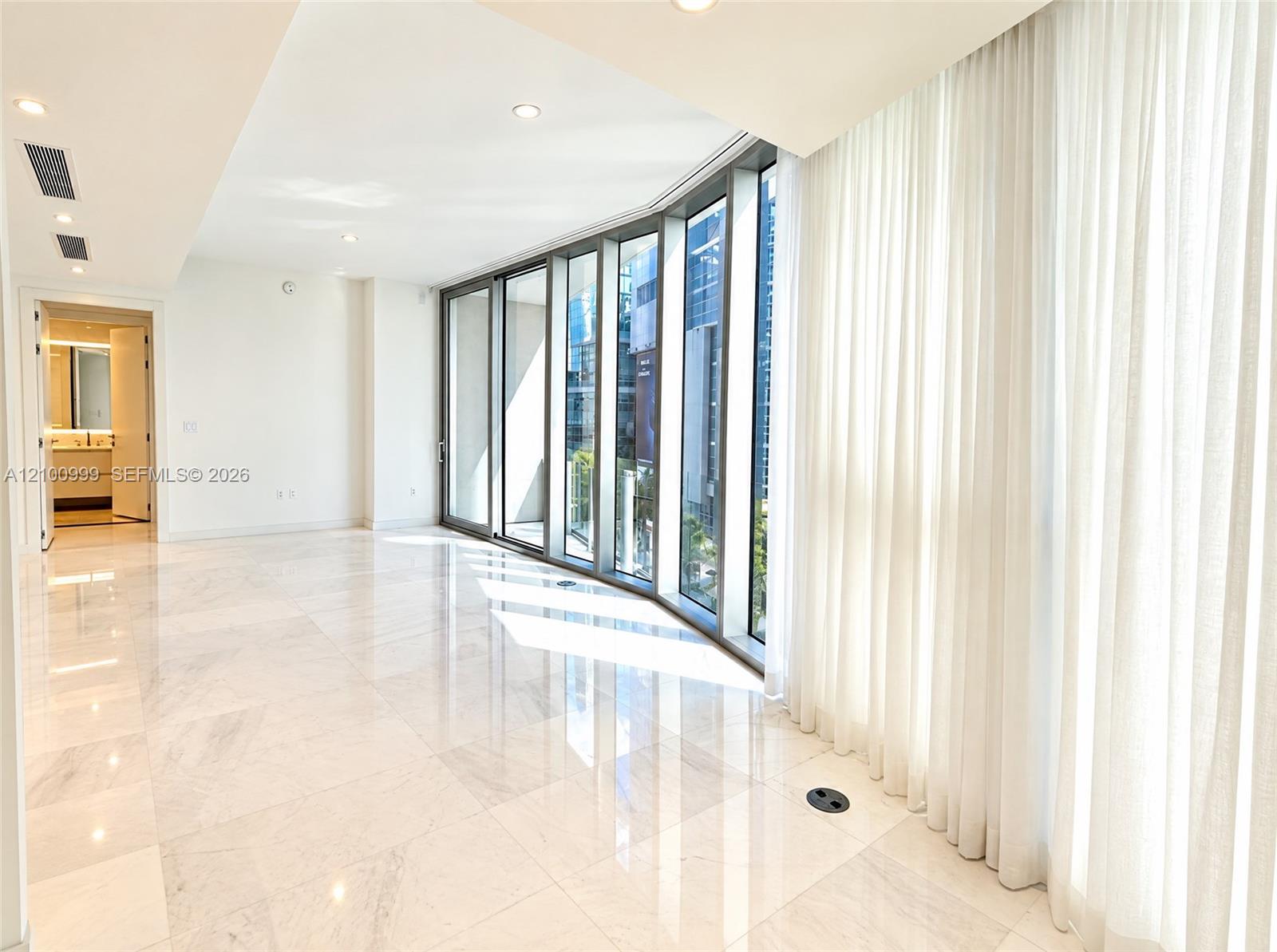 Vacant room with polished marble floors, curved floor-to-ceiling windows, and sheer curtains.