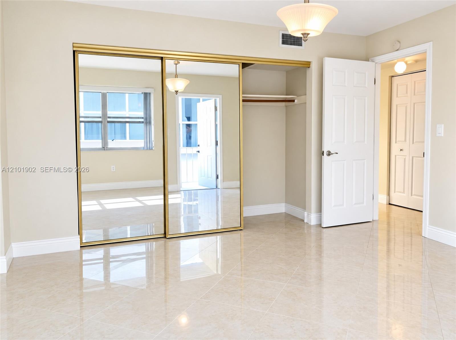 Vacant bedroom with glossy tile floors and mirrored gold-trimmed closet doors.