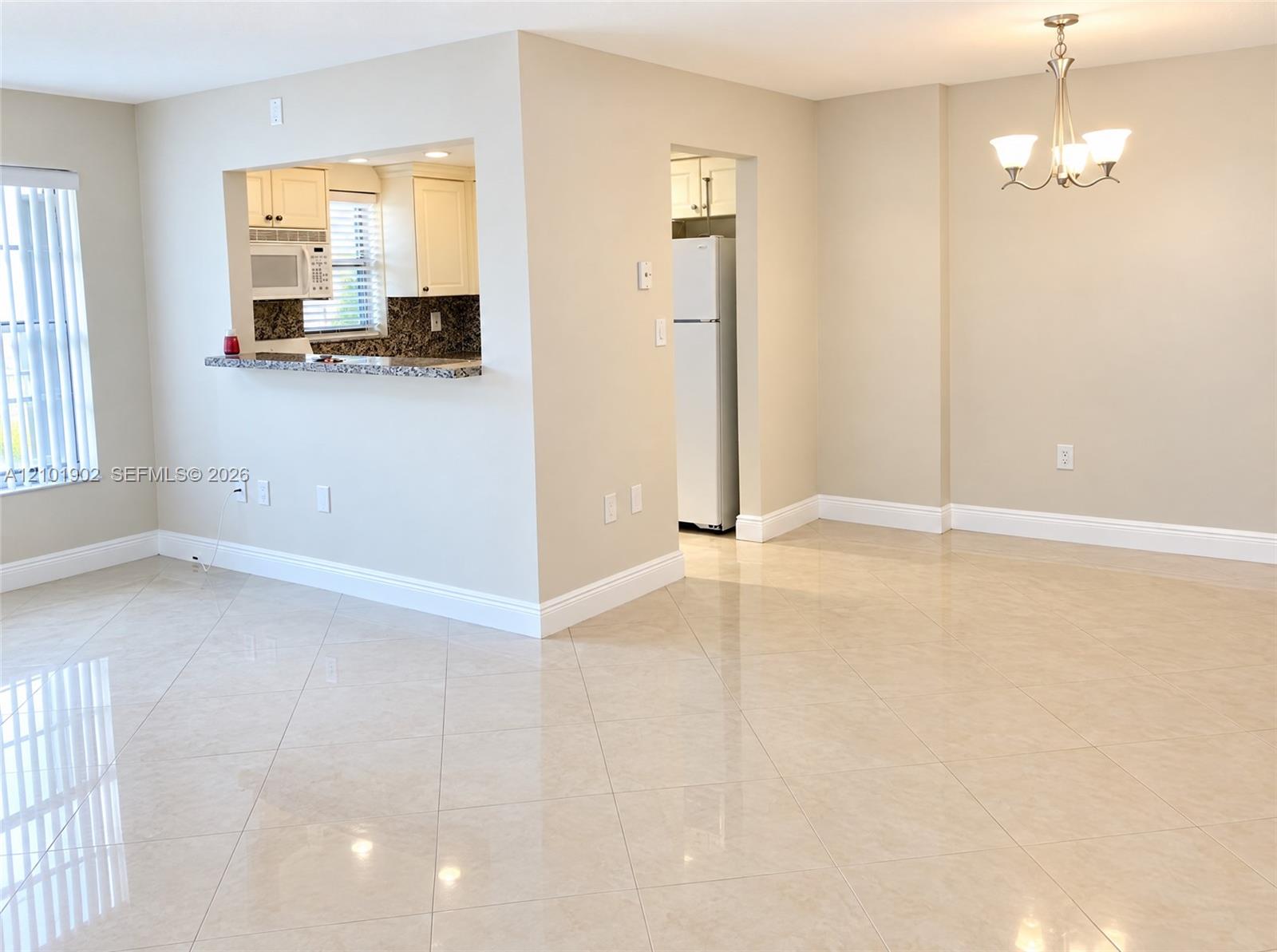 Unfurnished condo living and dining area with glossy tile floors, a kitchen pass-through, and a chandelier.