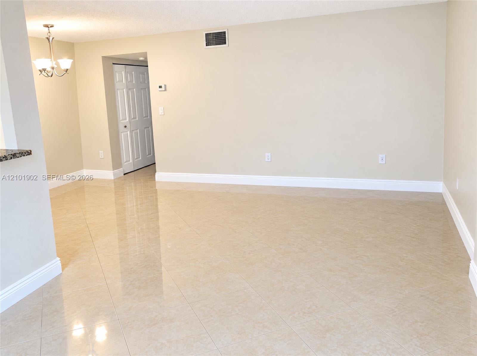 Vacant living area with glossy beige tile floors and a chandelier.