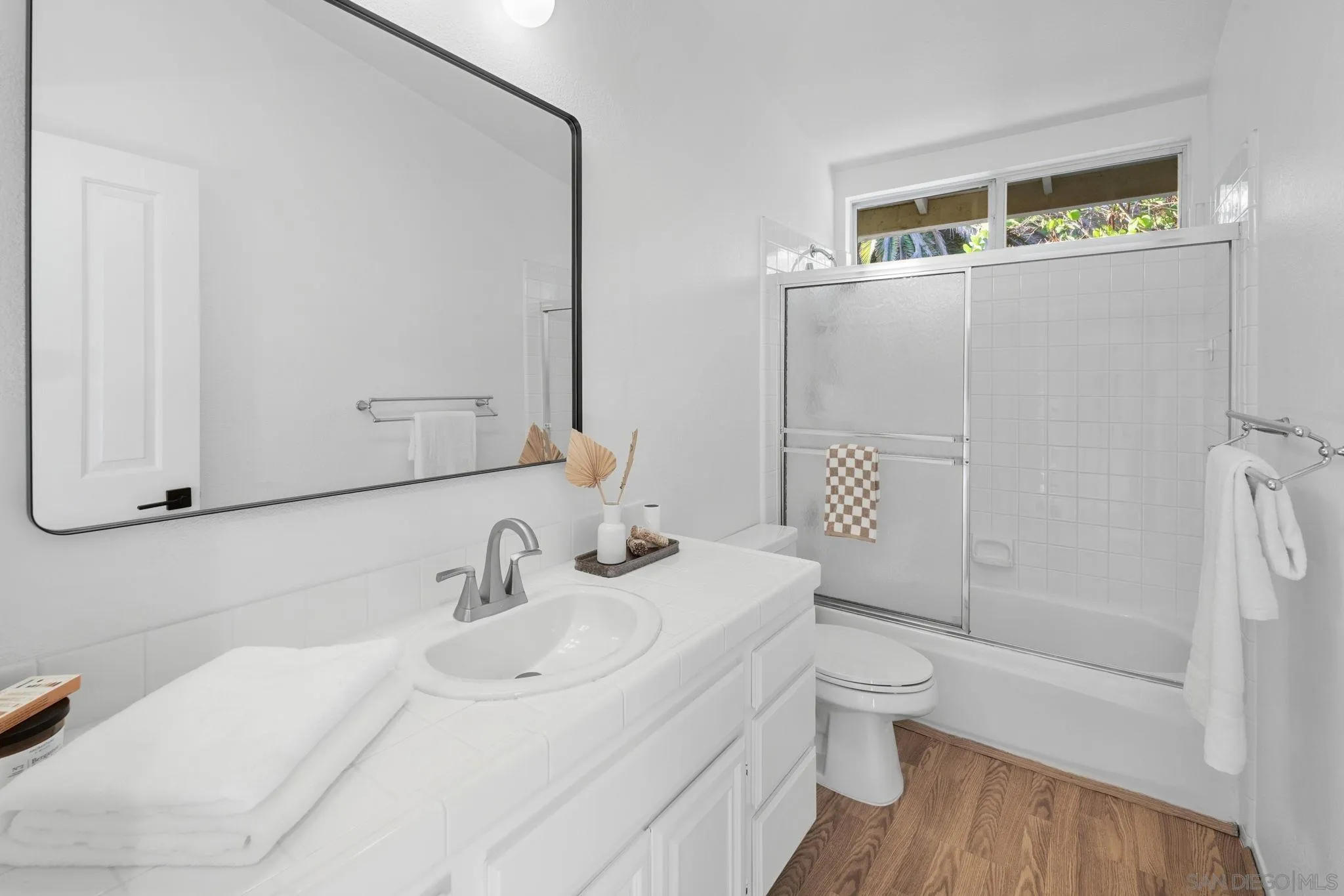 Bright white bathroom with a long vanity, black-framed mirror, and tiled tub and shower.
