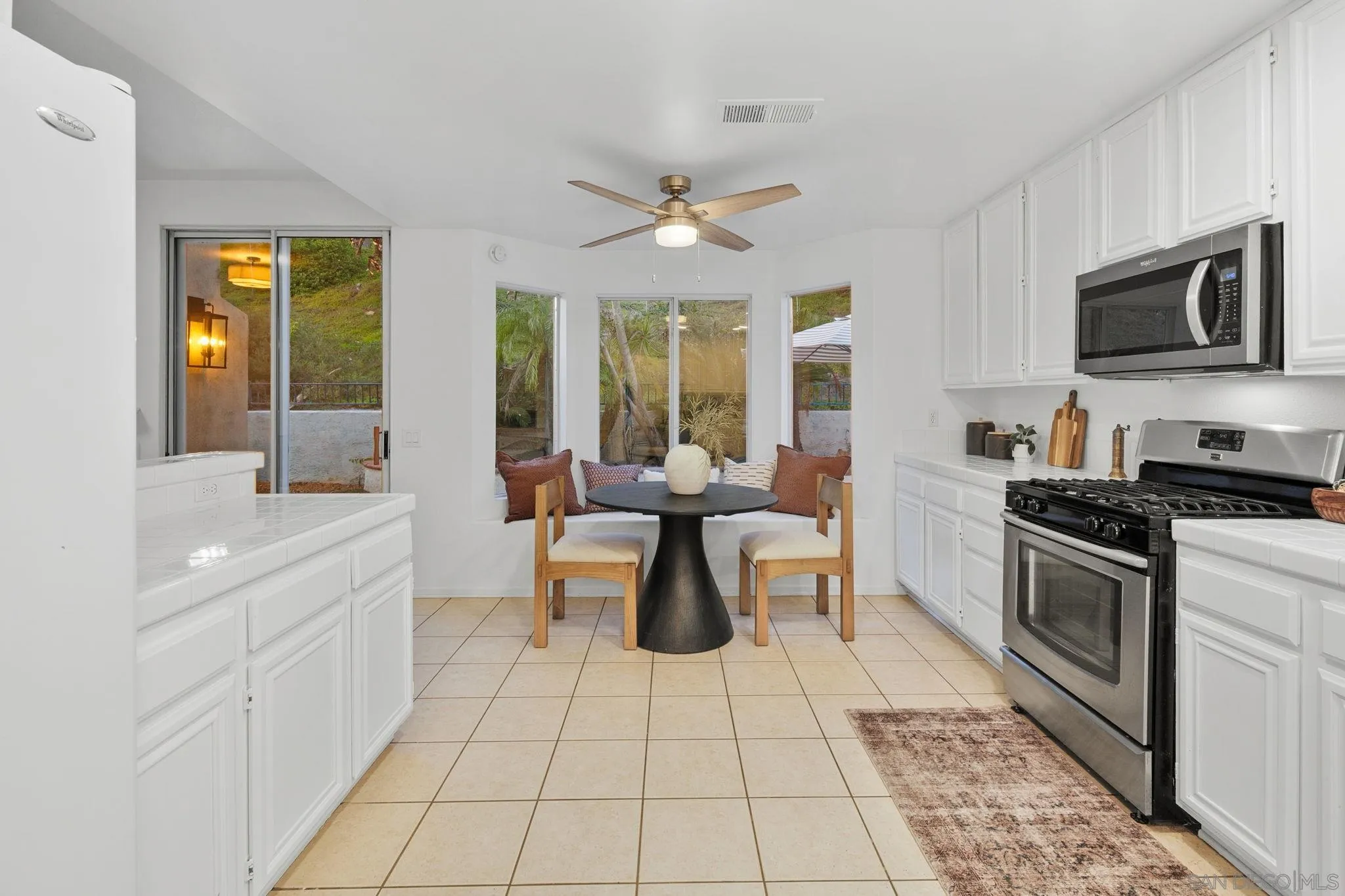 White kitchen with stainless steel appliances and a breakfast nook overlooking greenery.