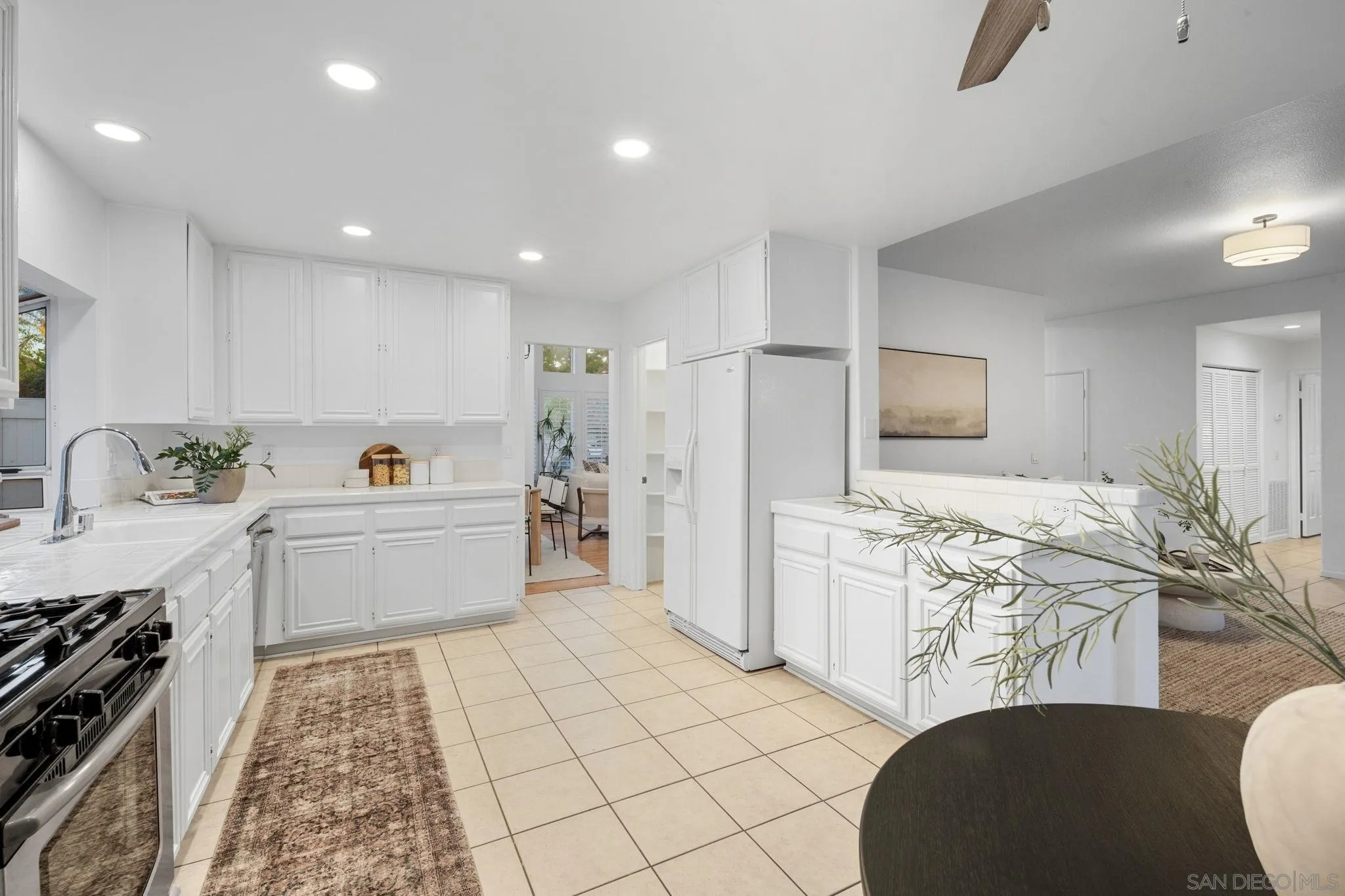 Bright white kitchen with tiled counters and floors, gas range, and open view into the living room.