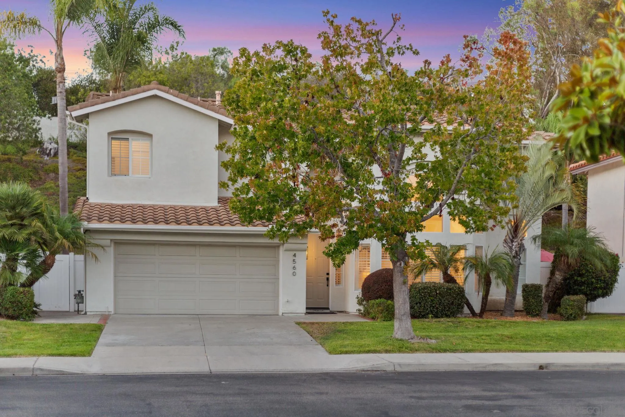 Two-story house with a double garage, tiled roof, and mature trees at dusk.