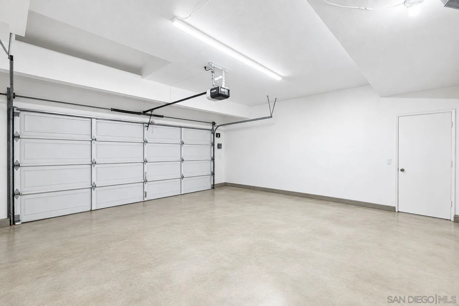 Empty garage with a wide sectional door, overhead opener, and separate side door.