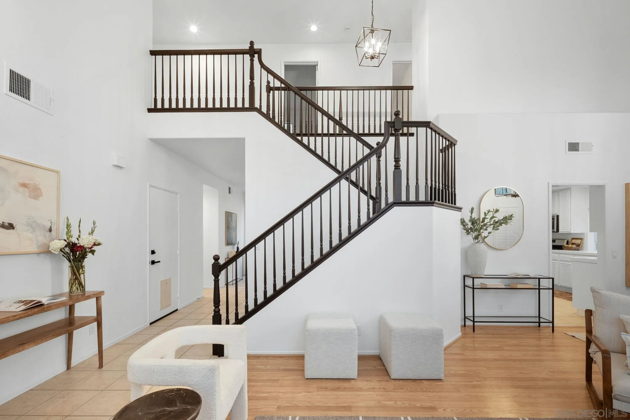 Staged home entry with a dark wood staircase, wood floors, and a glimpse of the kitchen.