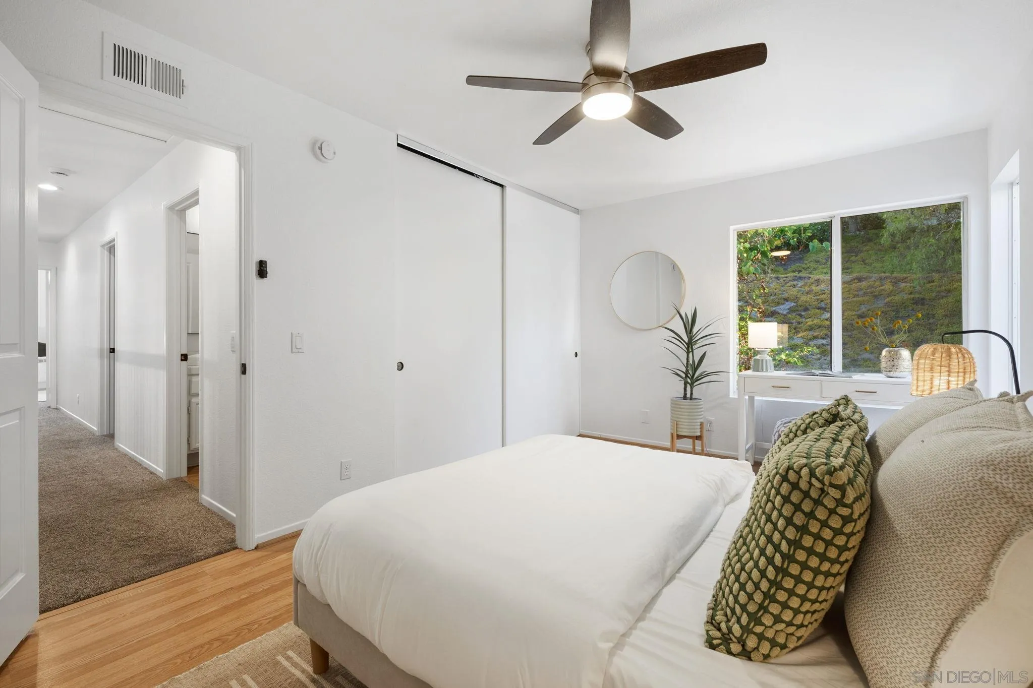 Bedroom with a white bed, green accent pillows, and a window facing a leafy hillside.