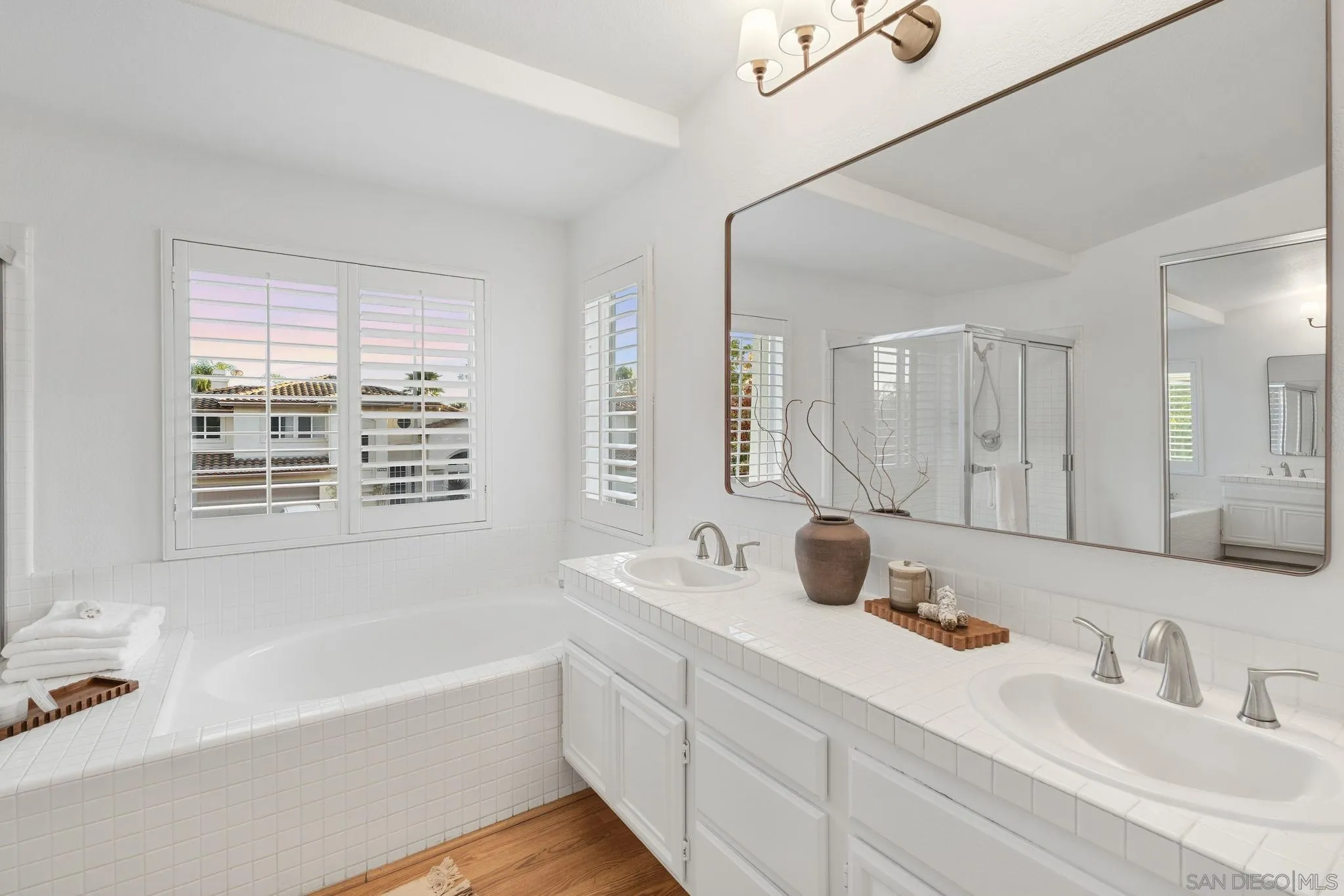 Bathroom with a tiled soaking tub, double vanity, and plantation-shuttered windows.