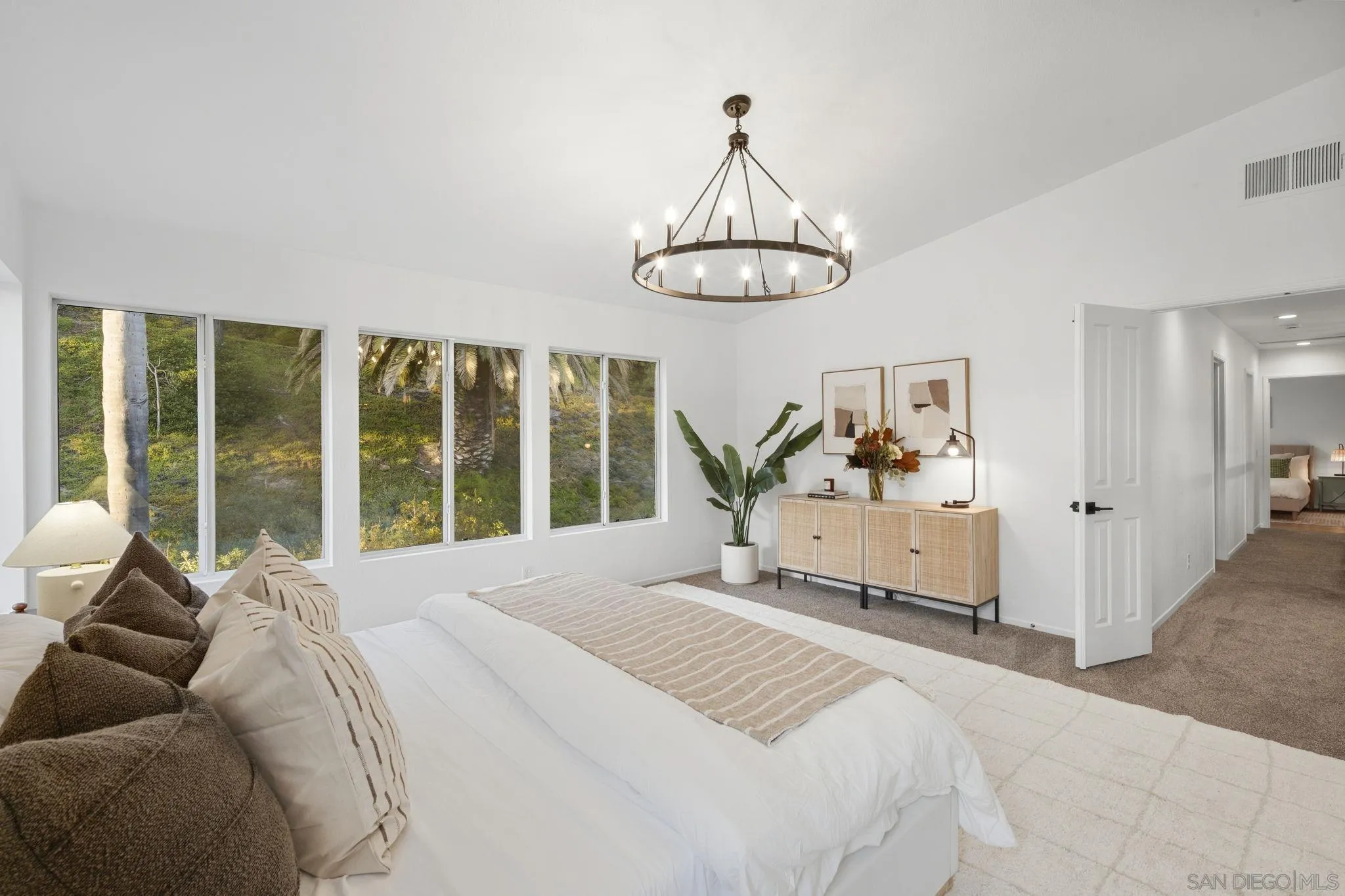 Staged bedroom with a large bed, garden-facing windows, and a circular chandelier.