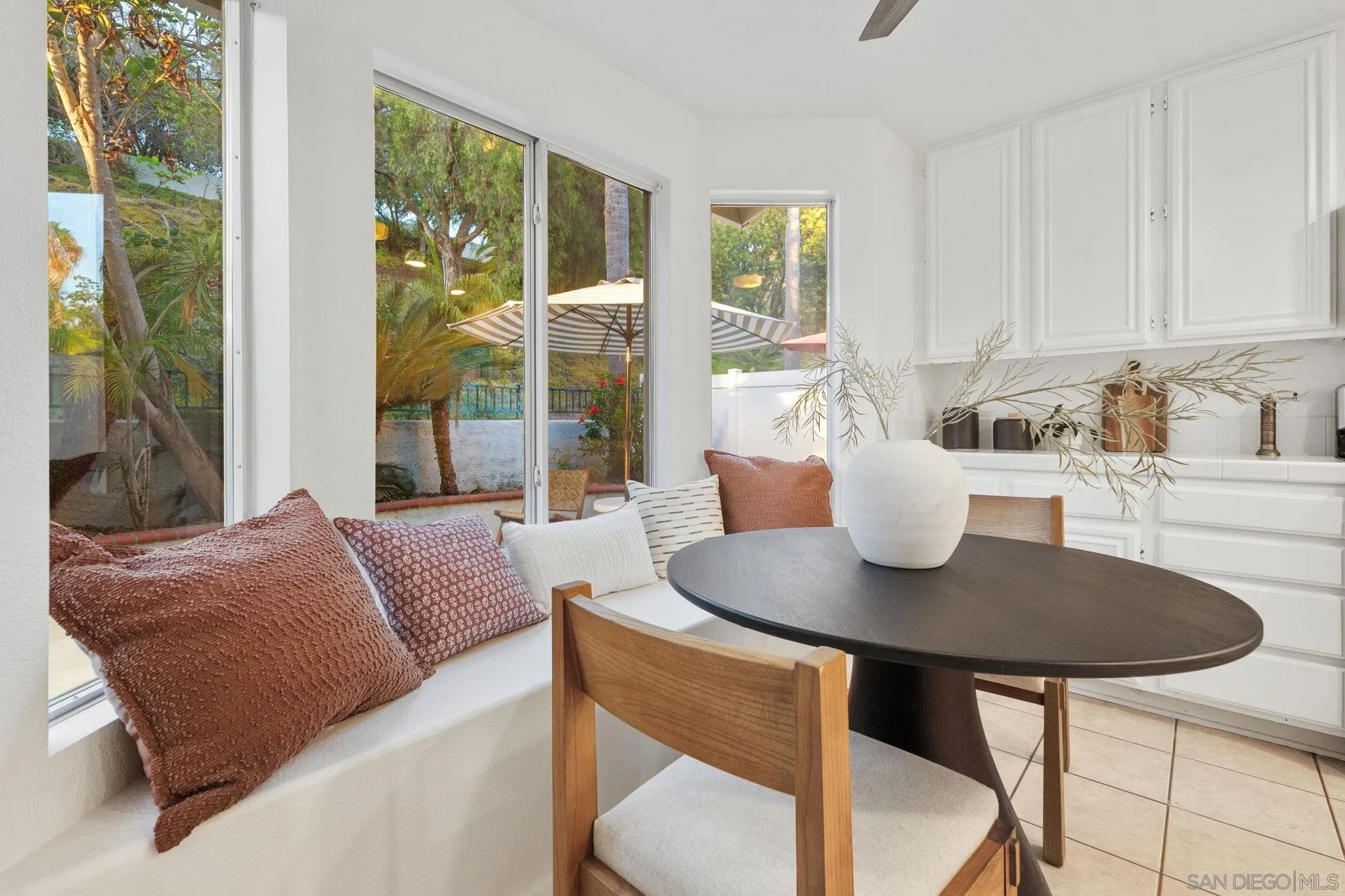 Dining nook with a window-seat bench, round table, white cabinetry, and views of a leafy patio.