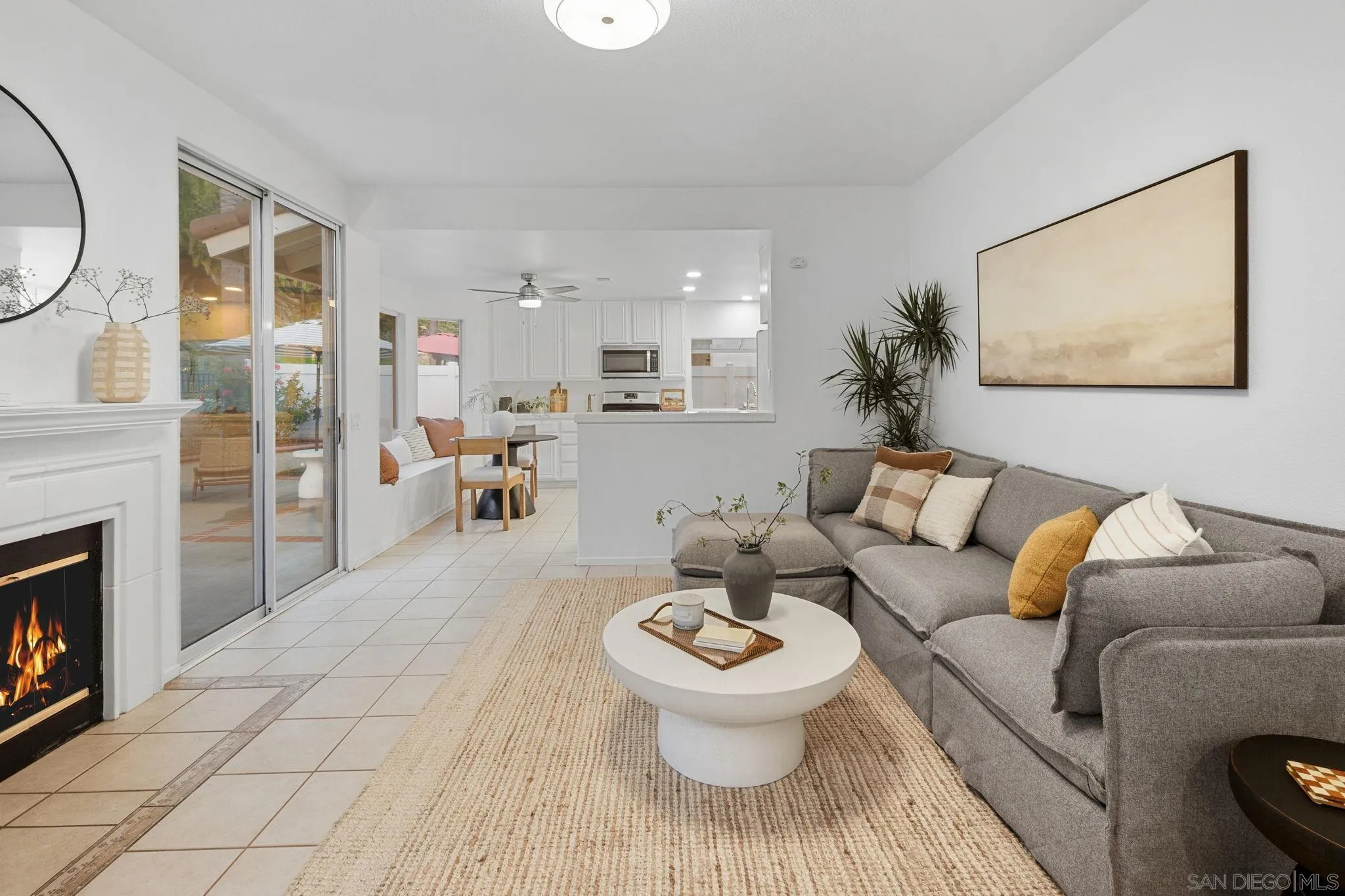 Staged living room with gray sectional, round coffee table, fireplace, and sliding doors beside an open kitchen.