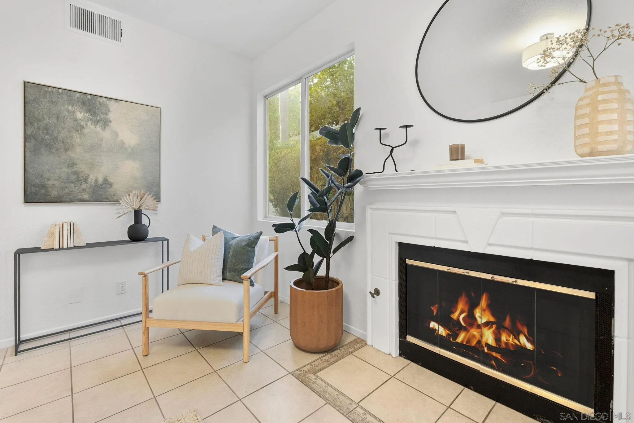 Staged living room with a lit fireplace and a cushioned armchair beside a tall potted plant.
