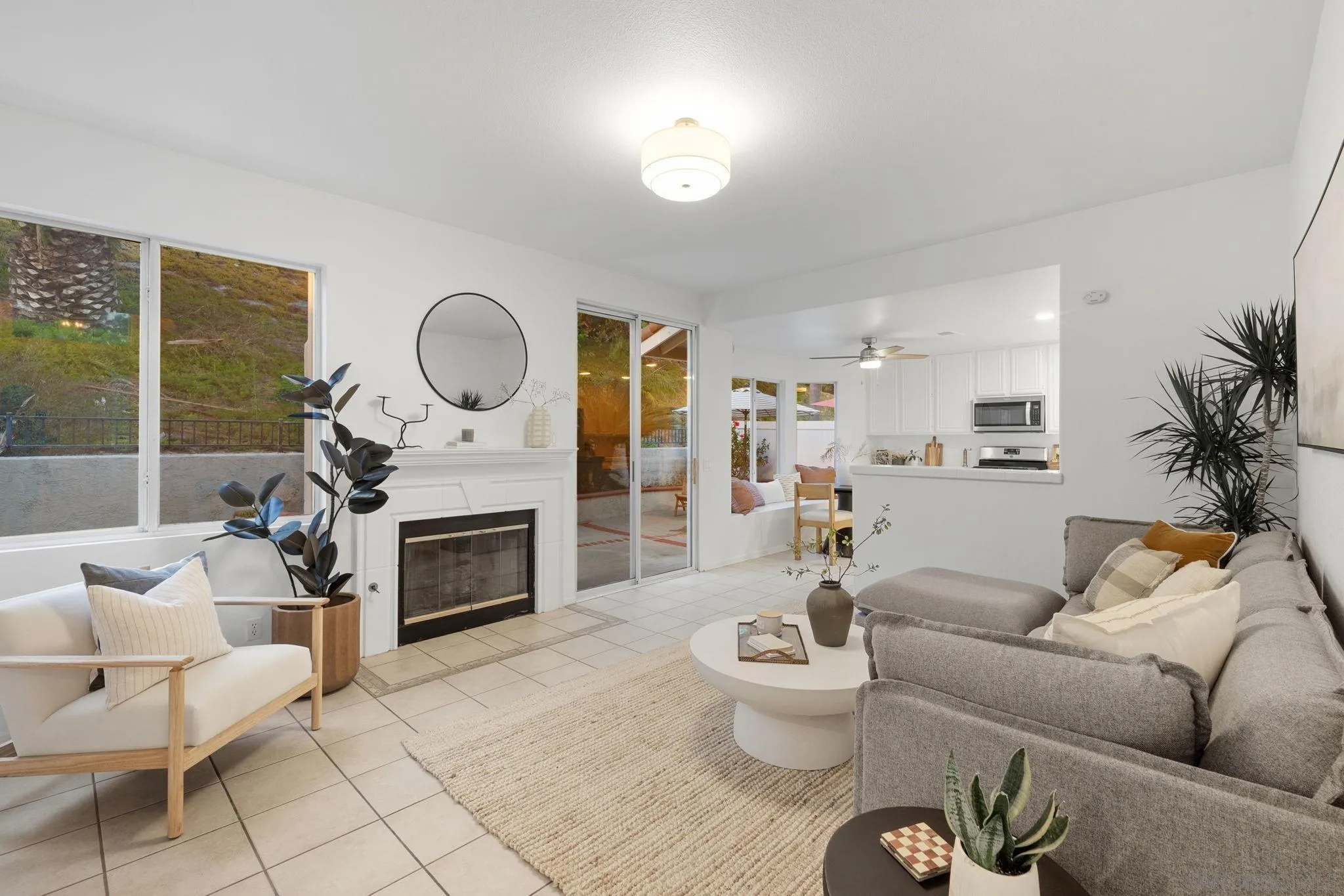 Staged living room with a white fireplace, gray sectional, and windows overlooking a hillside.