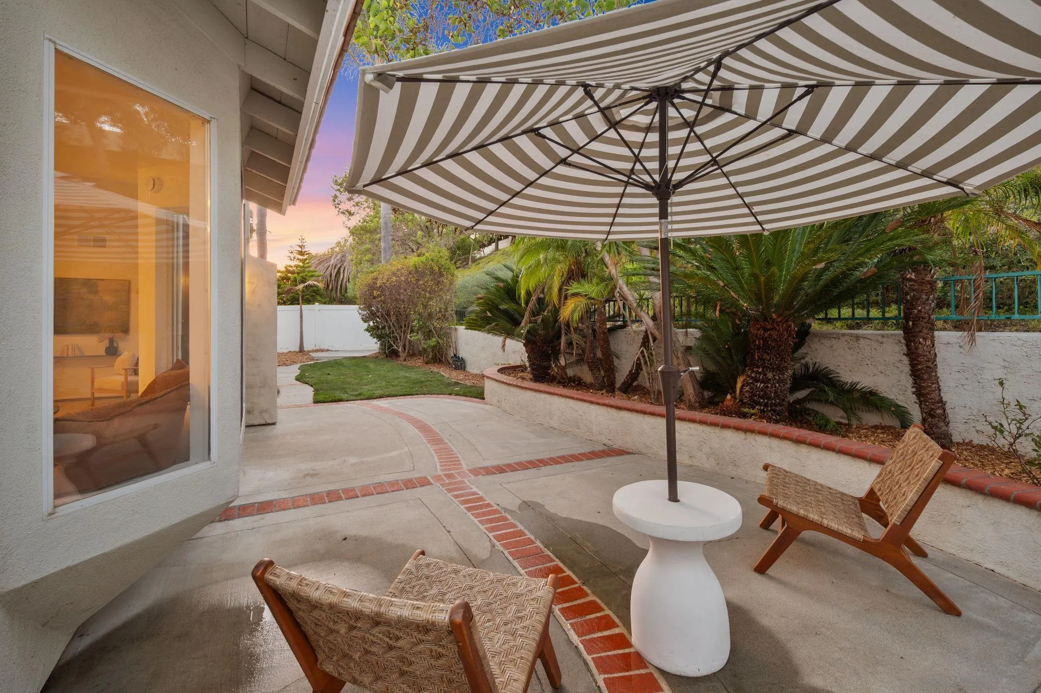 Backyard patio with a striped umbrella, wicker chairs, and a landscaped lawn.
