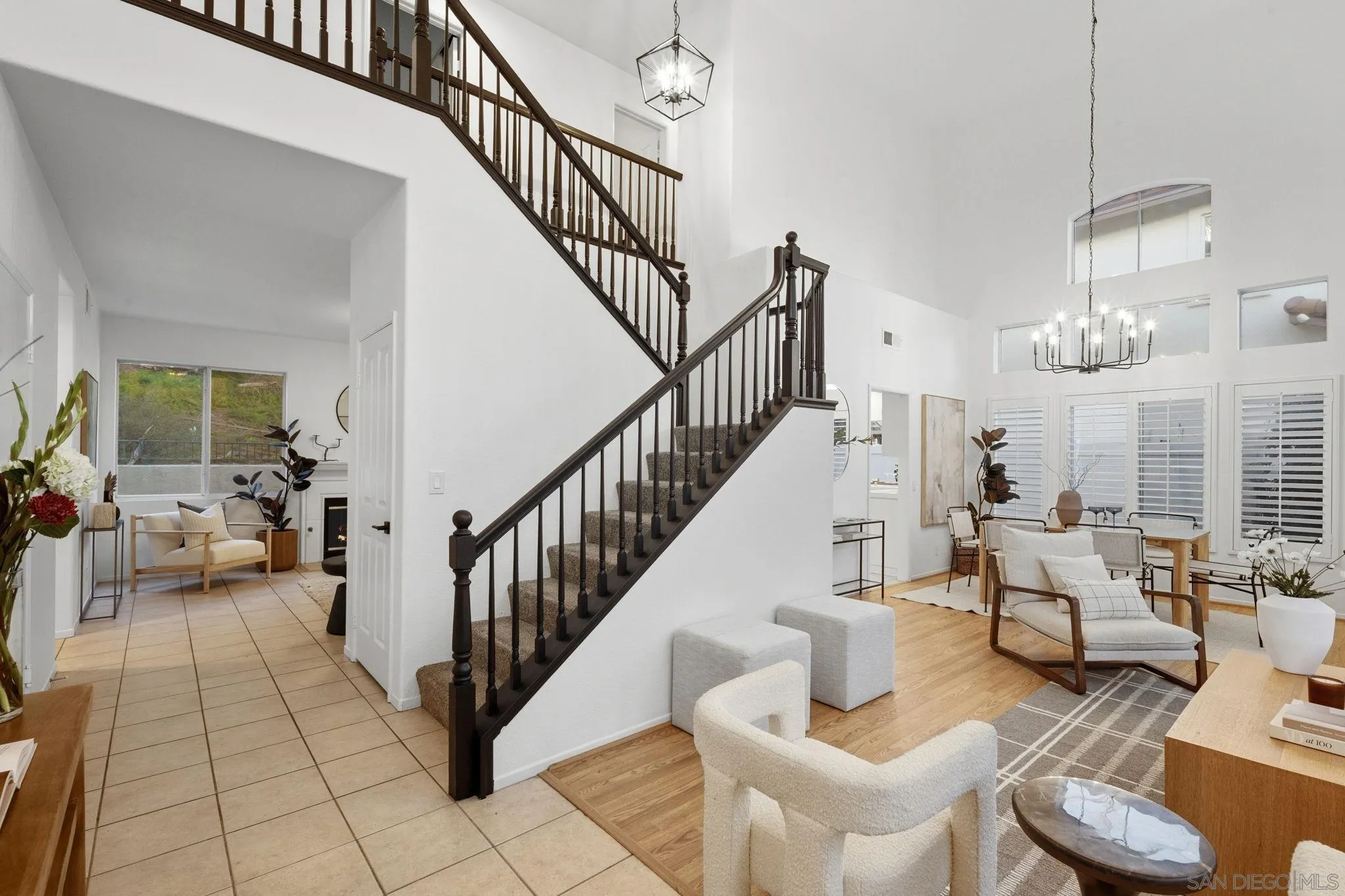 Open-plan living room with a dark wood staircase, vaulted ceiling, and plantation-shuttered windows.