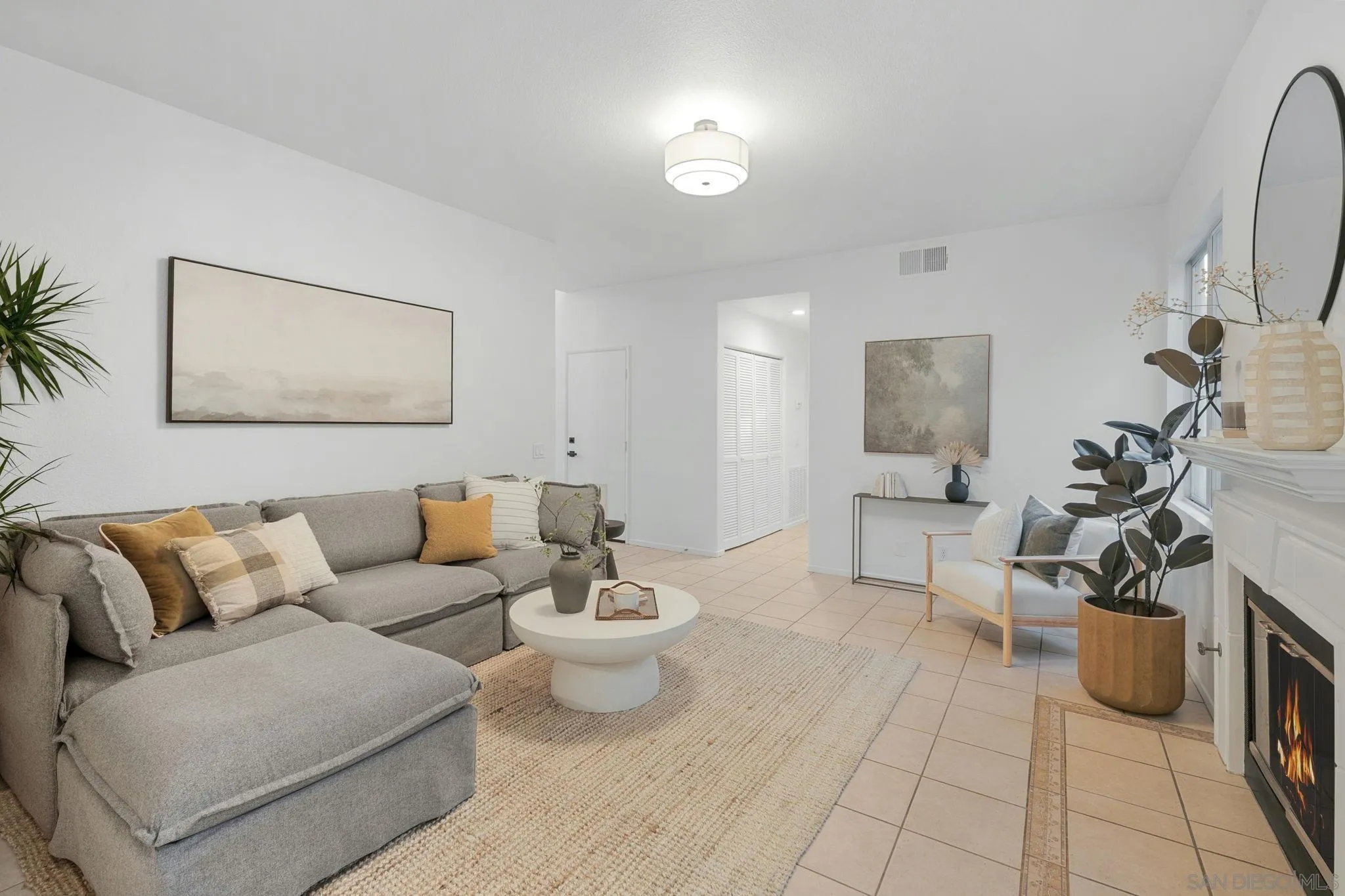 Staged living room with a gray sectional, round coffee table, and lit fireplace.