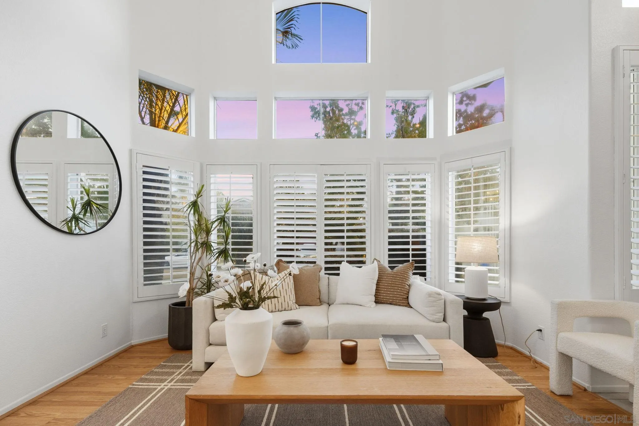 Living room with a white sofa and tall shuttered windows beneath clerestory windows.