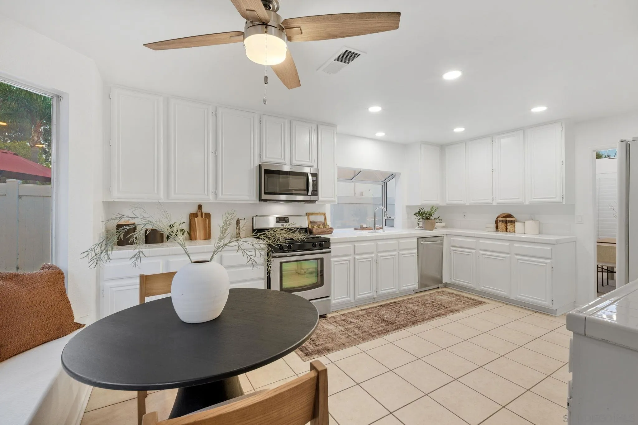 Bright white kitchen with stainless steel appliances and a round dining table in the foreground.