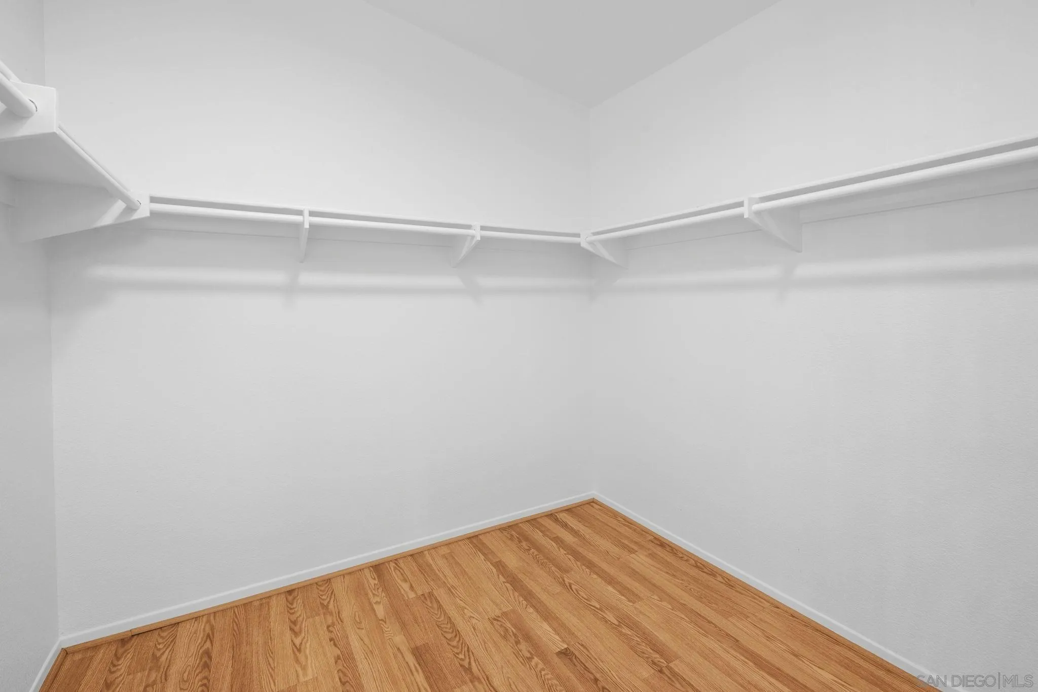 Empty walk-in closet with wraparound hanging rods and warm wood flooring.