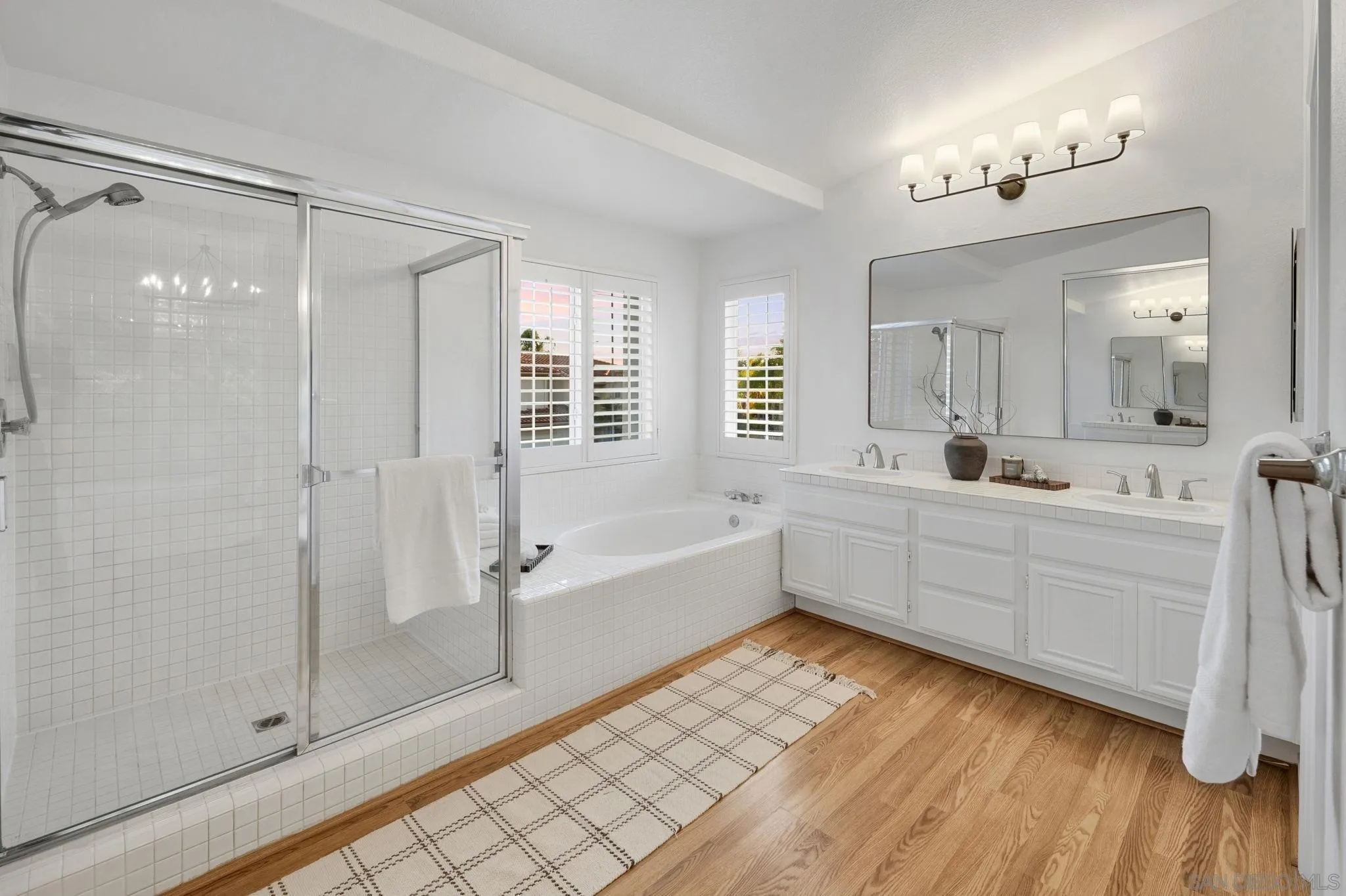Bathroom with a glass shower, built-in soaking tub, and long double-sink vanity.
