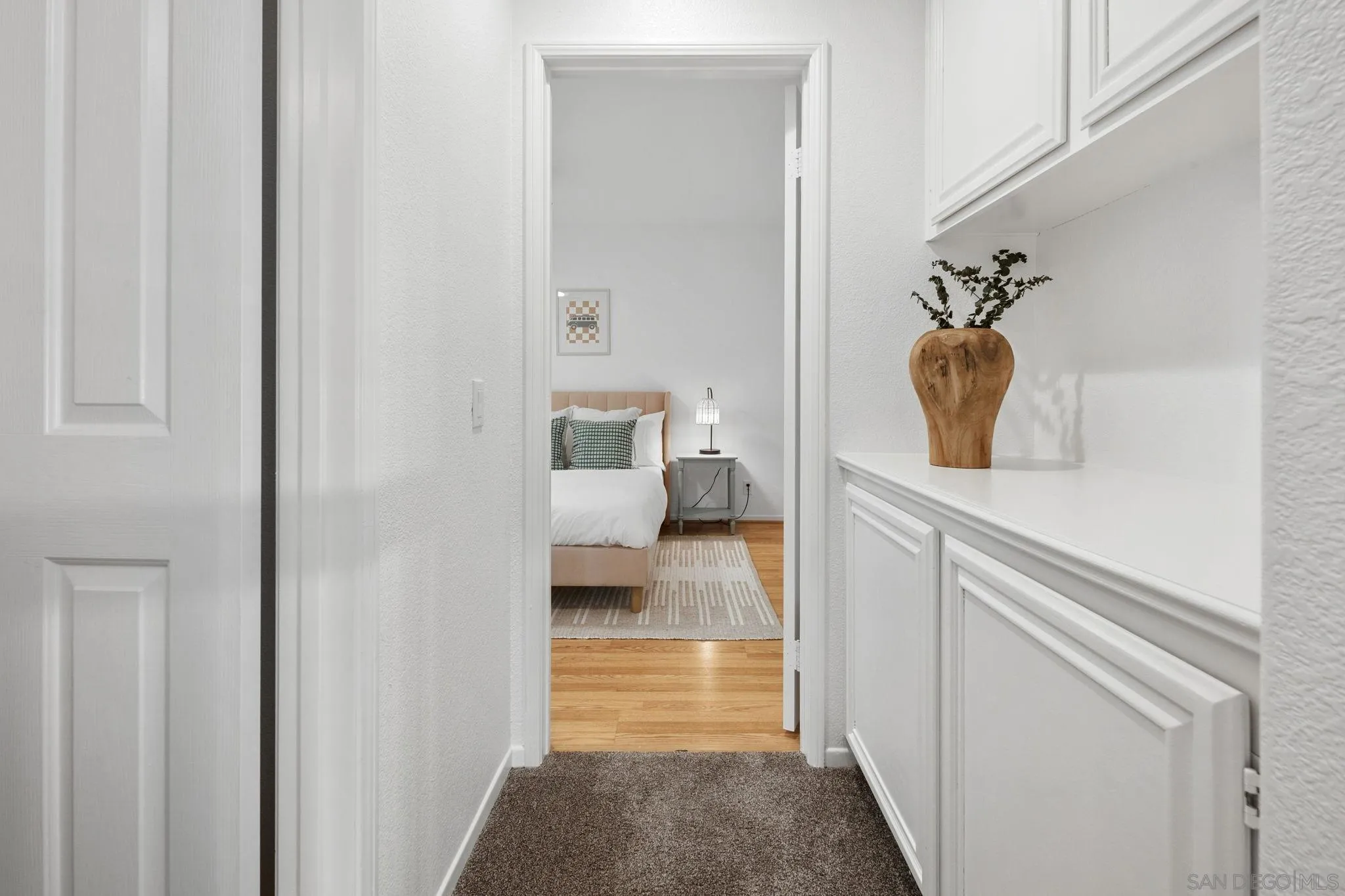 Hallway with white built-in cabinetry and a wooden vase, opening onto a staged bedroom.